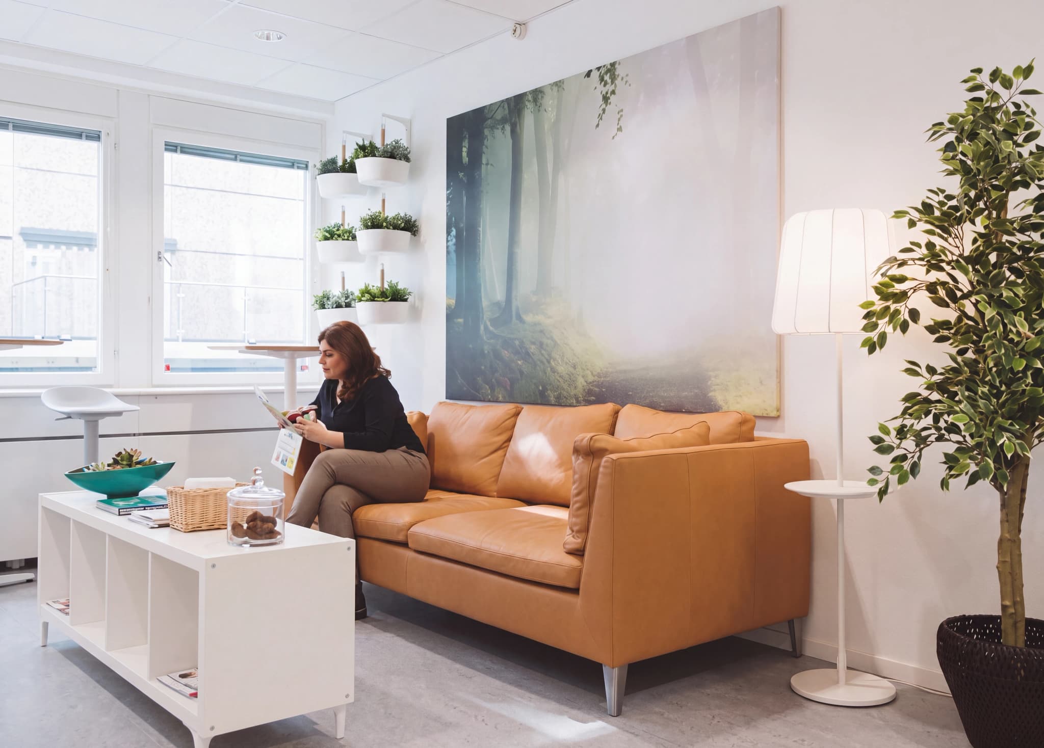 Kvinna sitter i en soffa och läser på en surfplatta i ett väntrum.