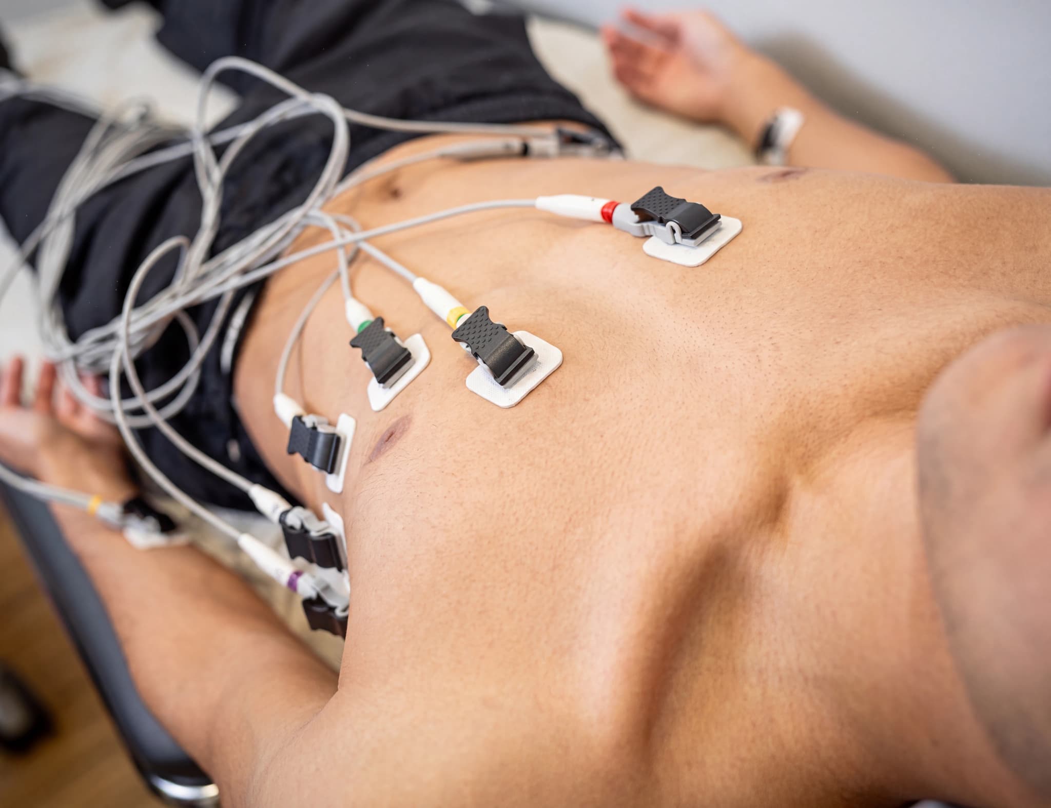 Patient ligger på en brits med EKG-elektroder fästa på bröstet, anslutna till sladdar.