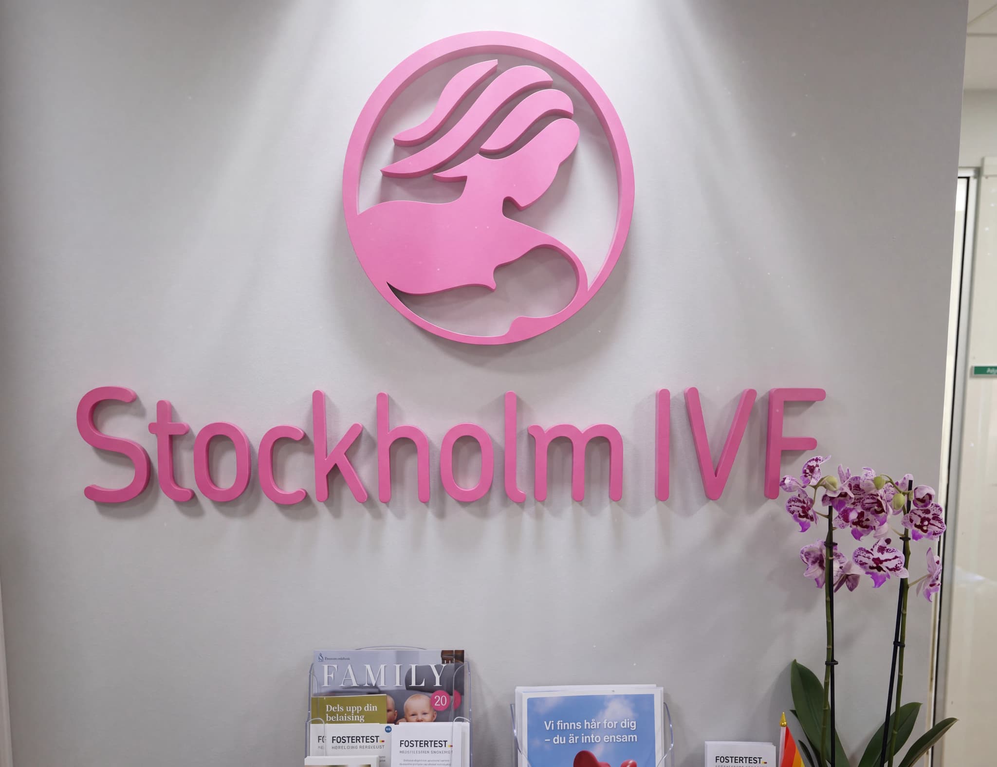 Logotyp för Stockholm IVF i rosa färg ovanför texten 'Stockholm IVF' och en orkidé i en mottagningslokal.