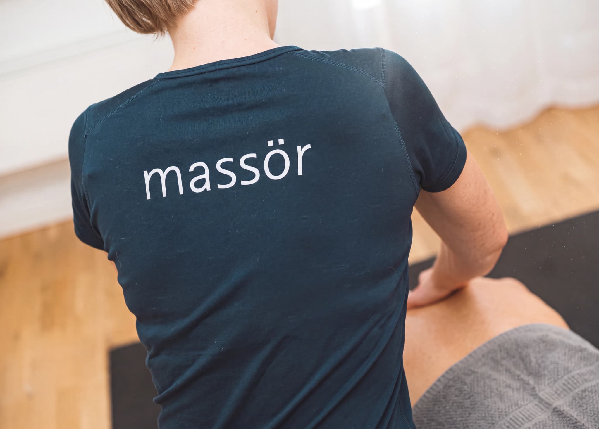 Massör med texten 'massör' på tröjan masserar en patients rygg.