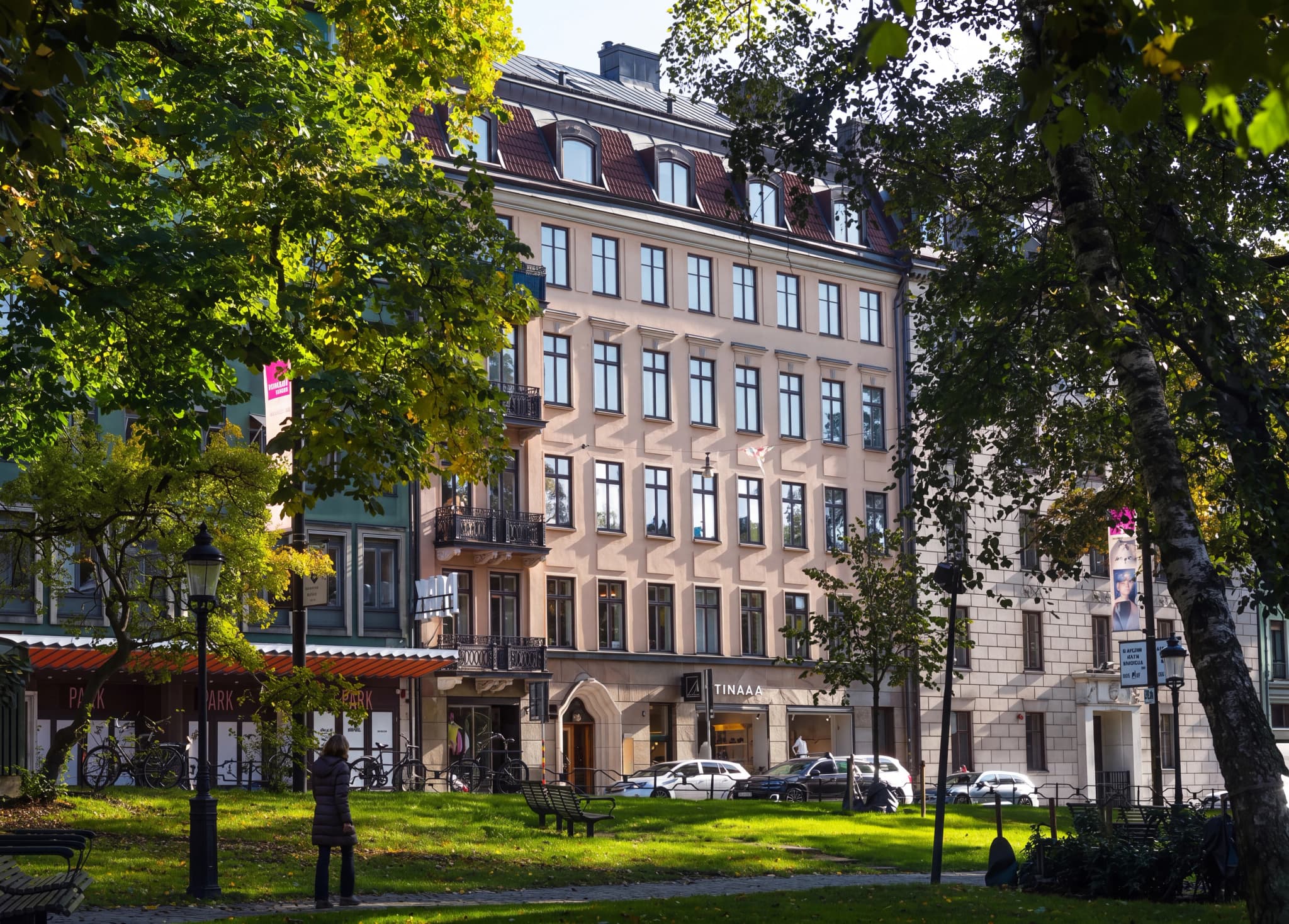 En byggnadsfasad med träd och grön park framför.