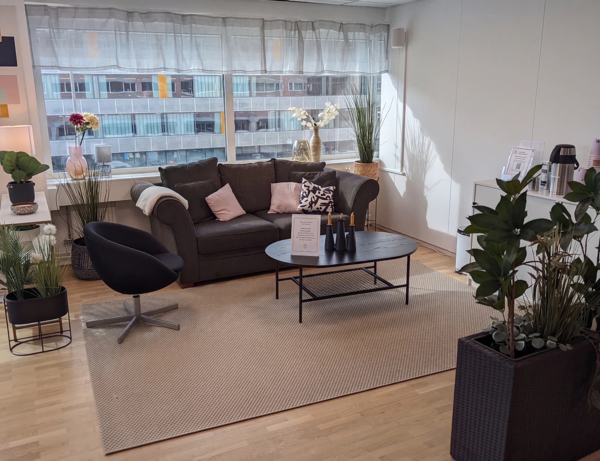 Ett väntrum med en mörk soffa, en svart fåtölj och ett runt soffbord.