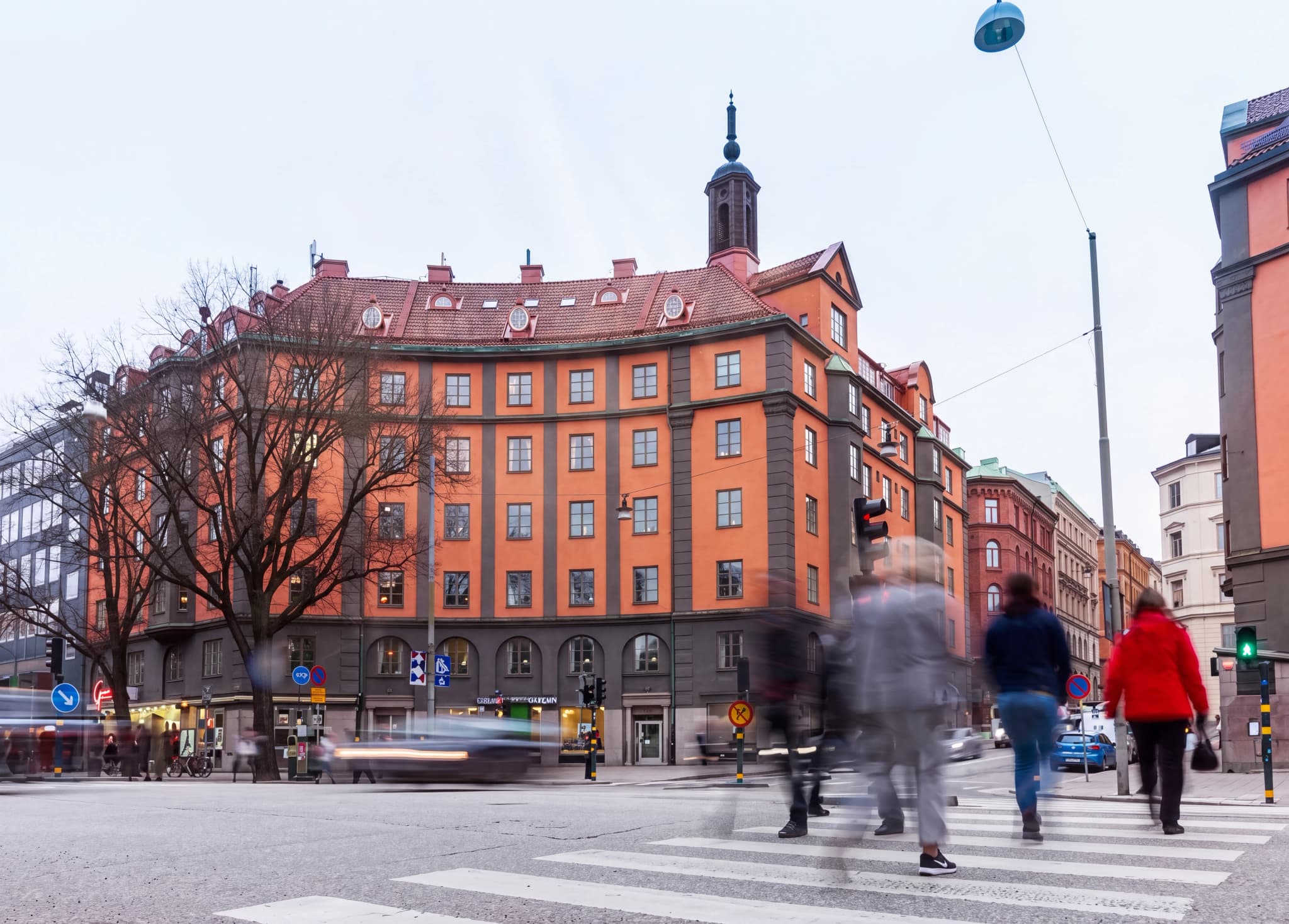 Människor korsar en gata vid ett övergångsställe i en stadsmiljö med byggnader i bakgrunden.
