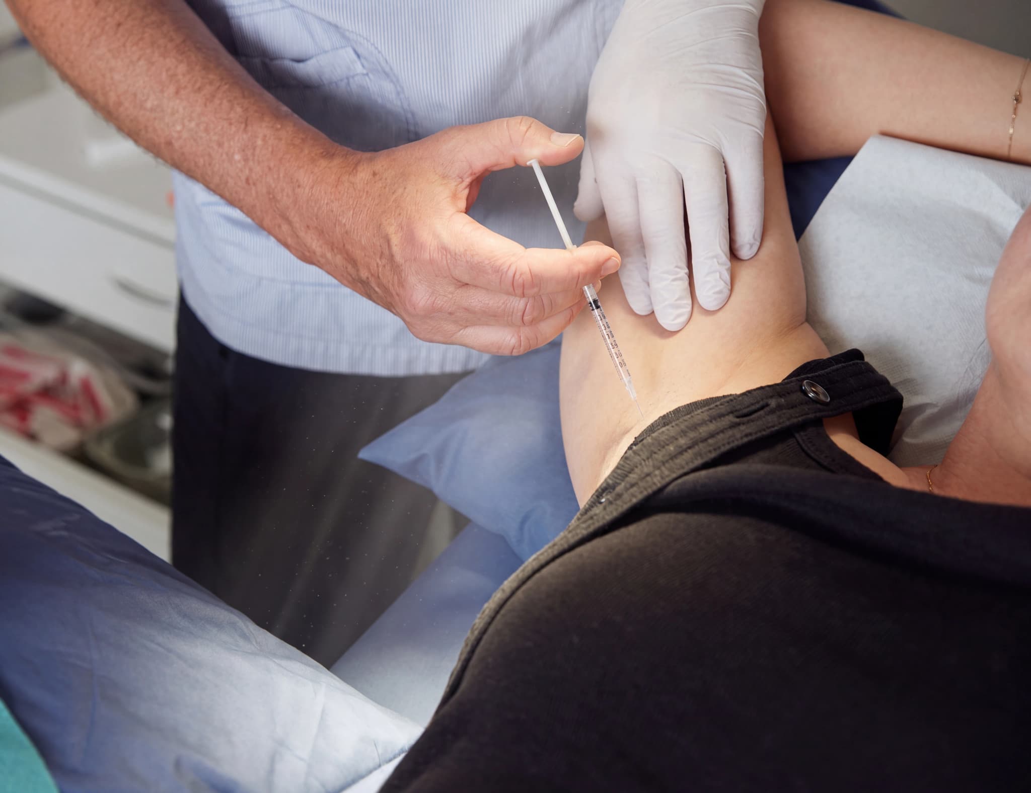 En person i vita handskar administrerar en injektion i armen på en patient.