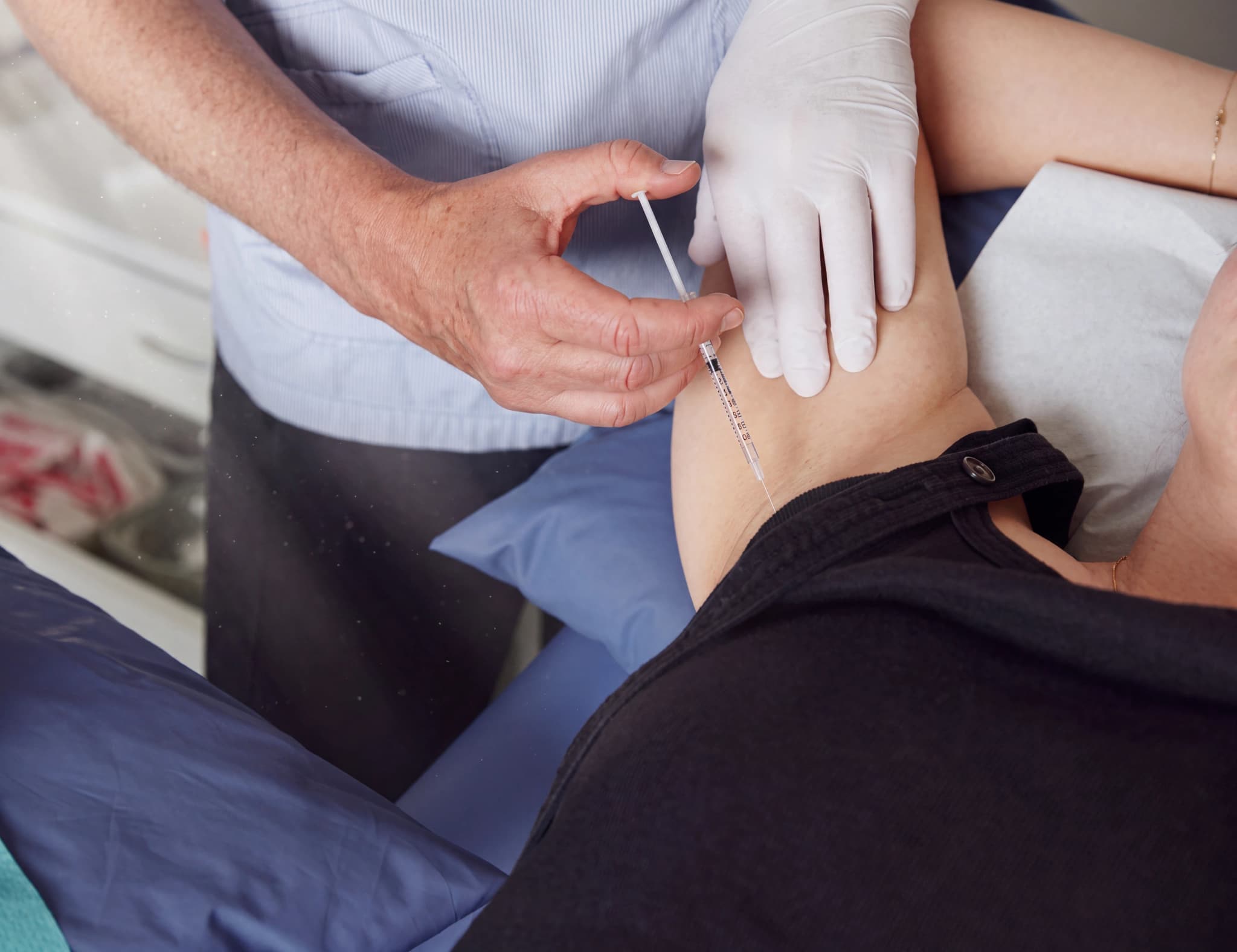 Läkare i handskar injicerar en patientens arm medan patienten ligger i en säng.