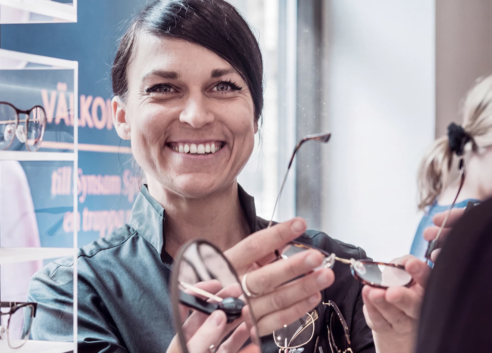 Optiker ler och visar ett par glasögon för en kund i en butik.