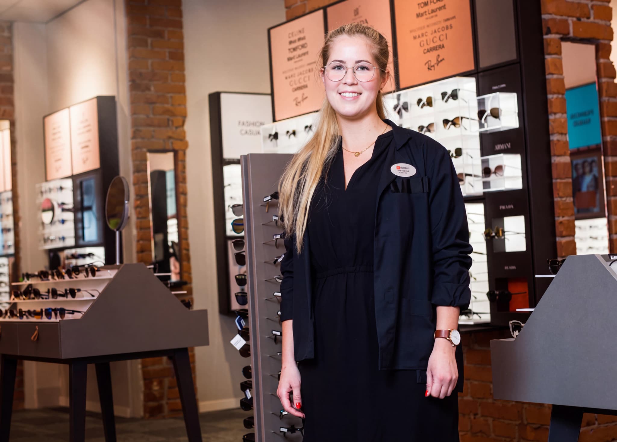 En kvinna som arbetar som optiker står i en butik som säljer glasögon och solglasögon.