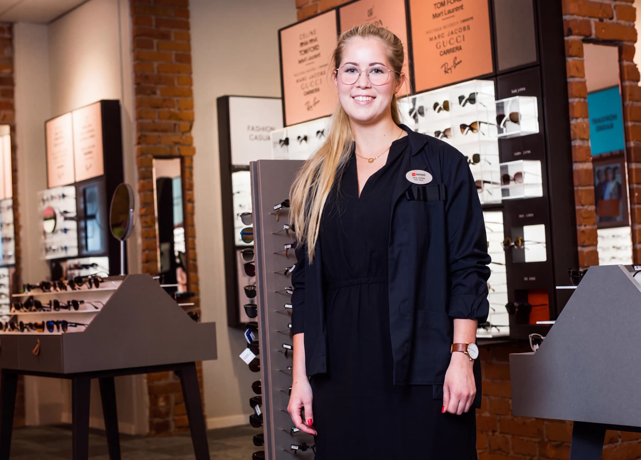 Optiker i glasögonbutik med displayer av glasögon.