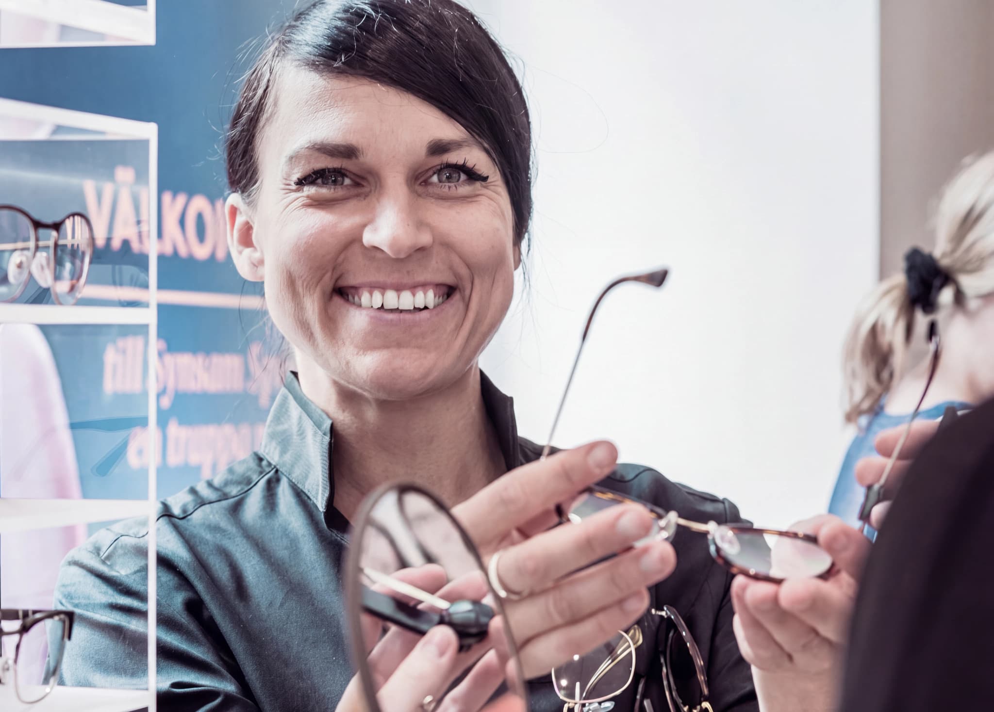 En leende optiker visar glasögon för en kund i butiken.