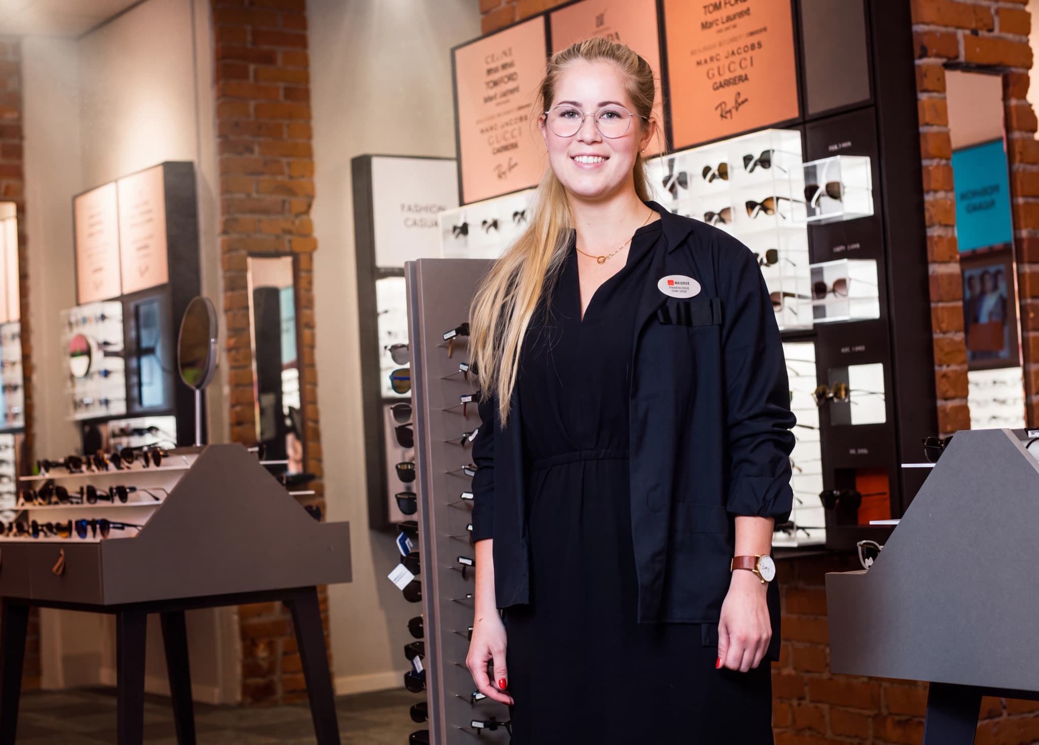 En ung kvinna med glasögon står i en butik som säljer glasögon och solglasögon.