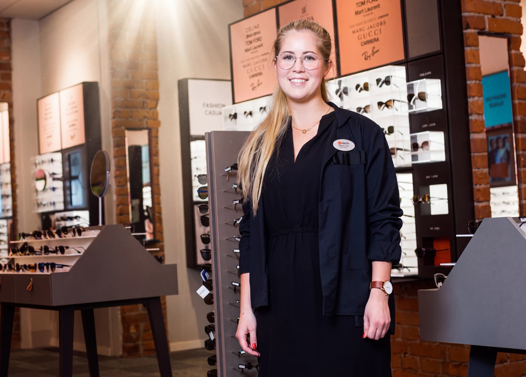 Optiker ler och visar upp glasögon i en butik.