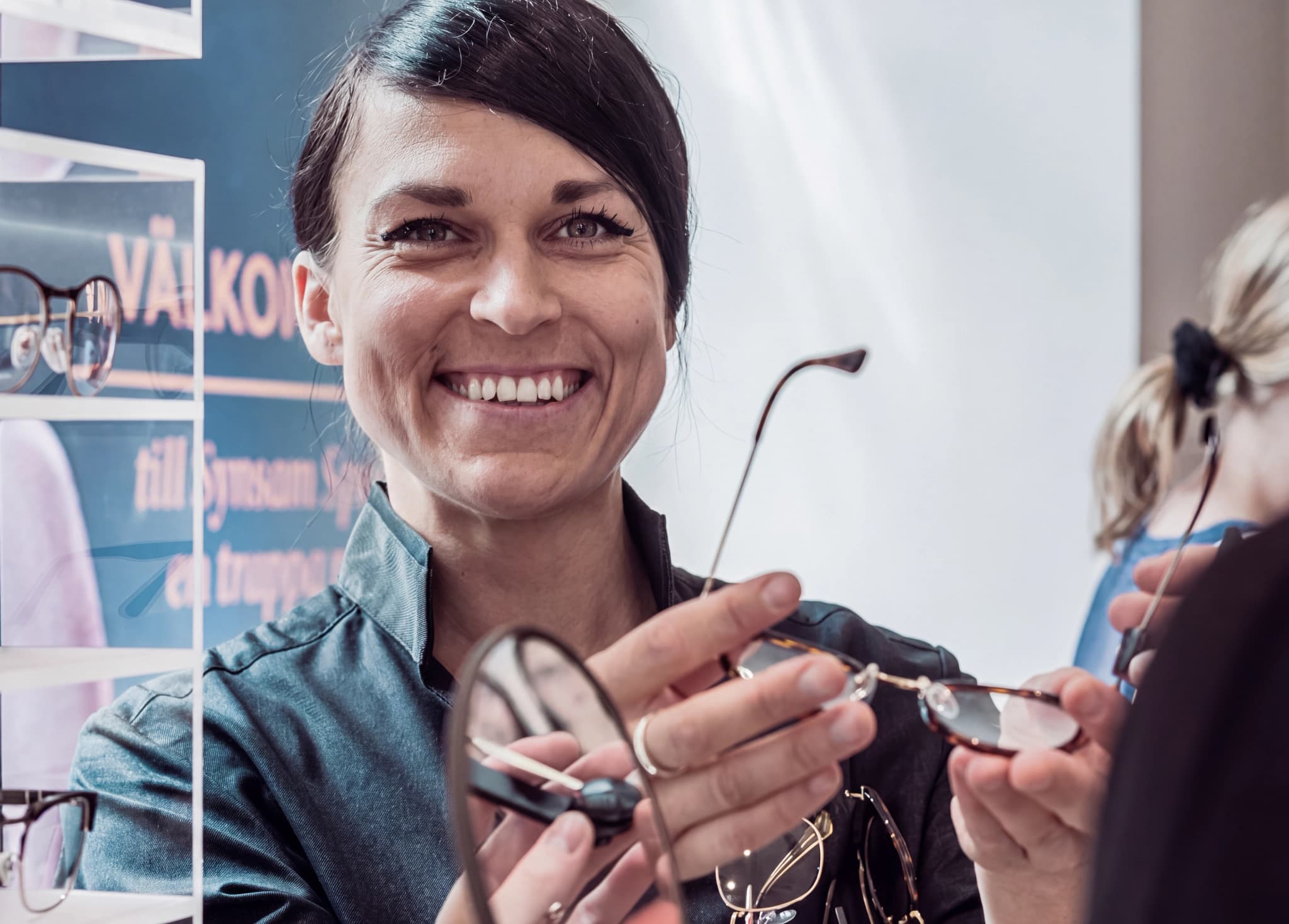 En leende optiker visar ett par glasögon för en kund i en butik.
