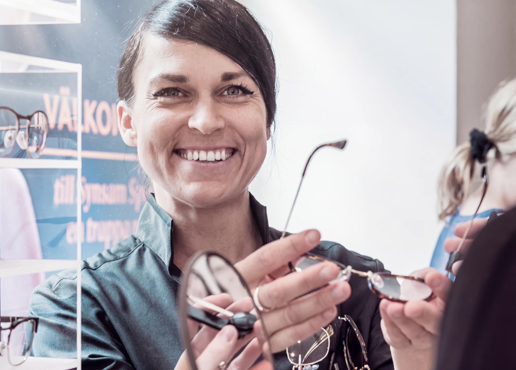 En leende optiker visar upp ett par glasögon för en kund i butik.