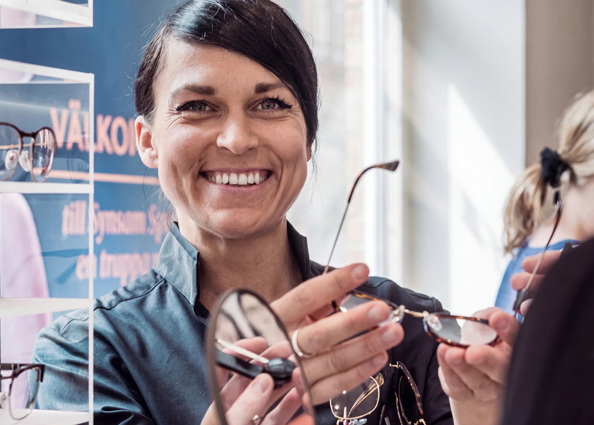 Optiker ler och visar glasögon för en kund i en butik.