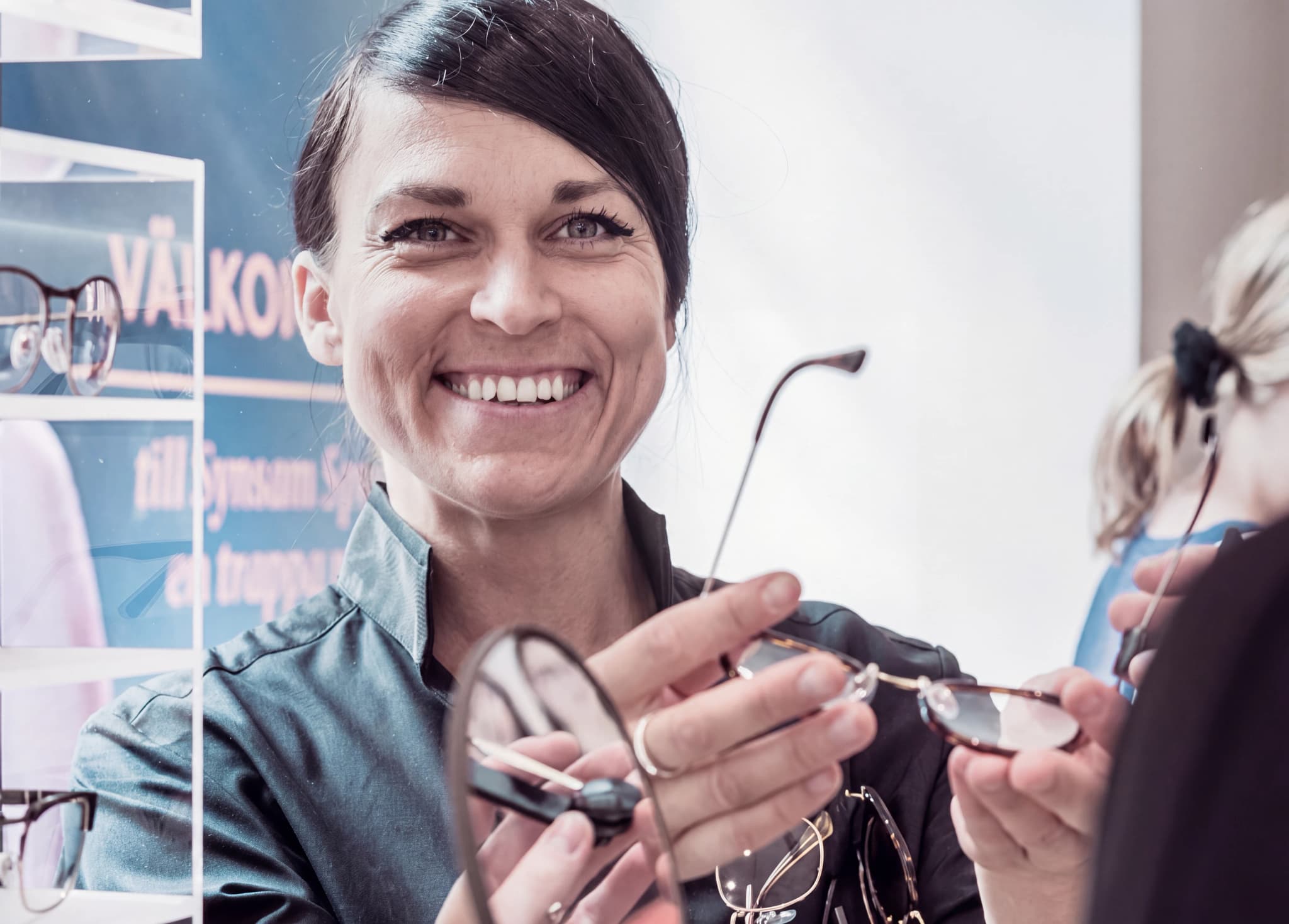 Optiker ler och visar upp glasögon för en kund i en butik.