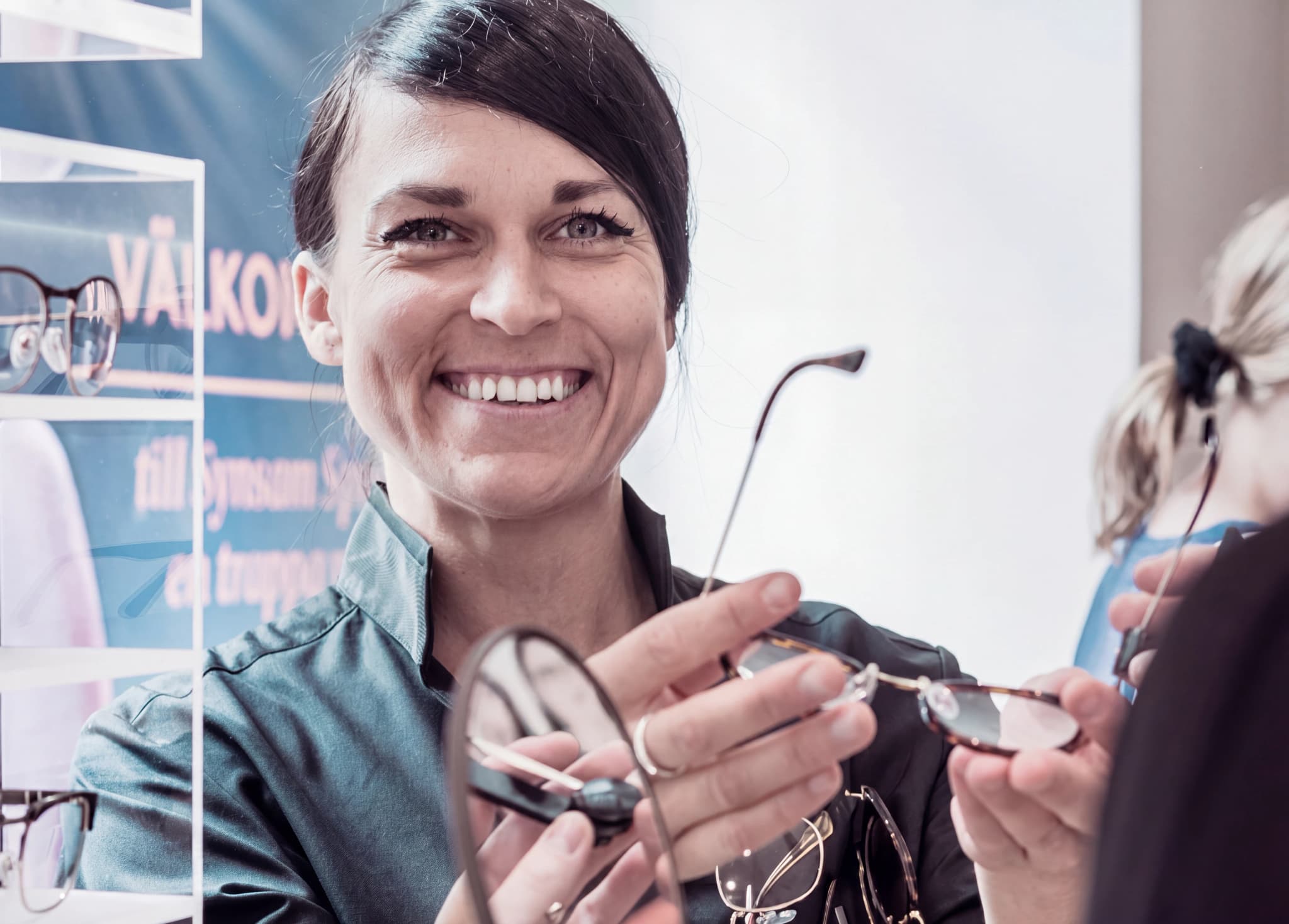 Optiker visar upp glasögon för en kund, med ett leende i butiksmiljö.