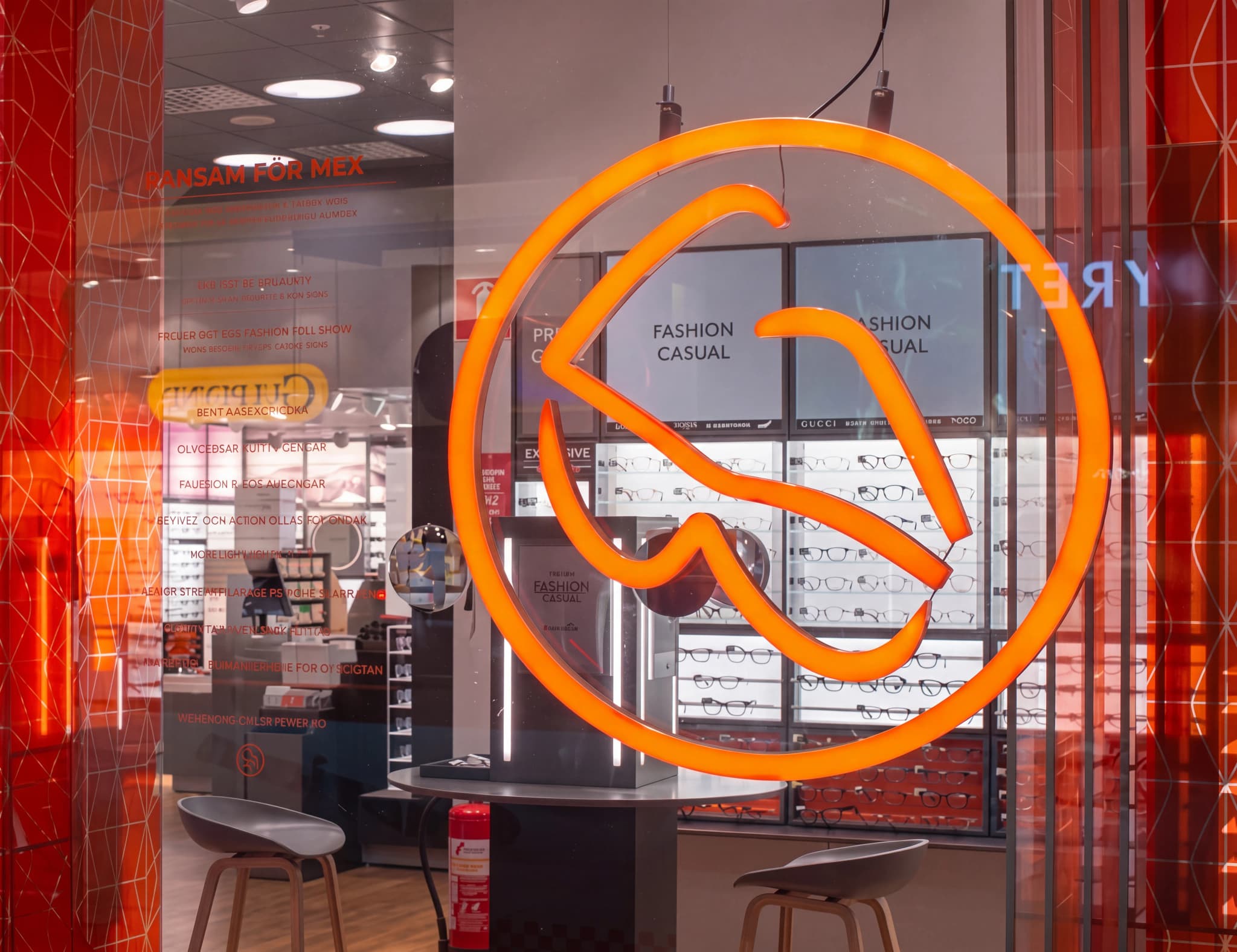 En närbild av en butiksfasad med en orange neonlogotyp i form av glasögon och fönstervisningar med glasögon.