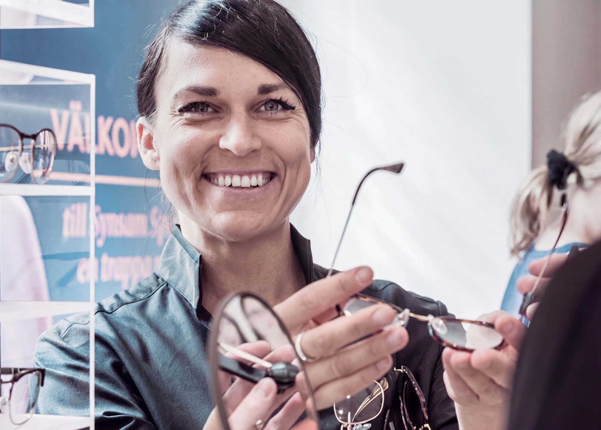 Optiker visar ett par glasögon för en kund i en butik.