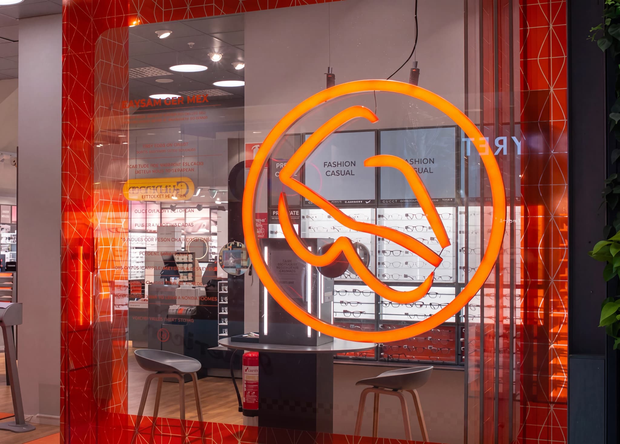 Framsidan av en optikaffär med en stor neonlogotyp som formar glasögon och hyllor med glasögon bakom glasrutan.