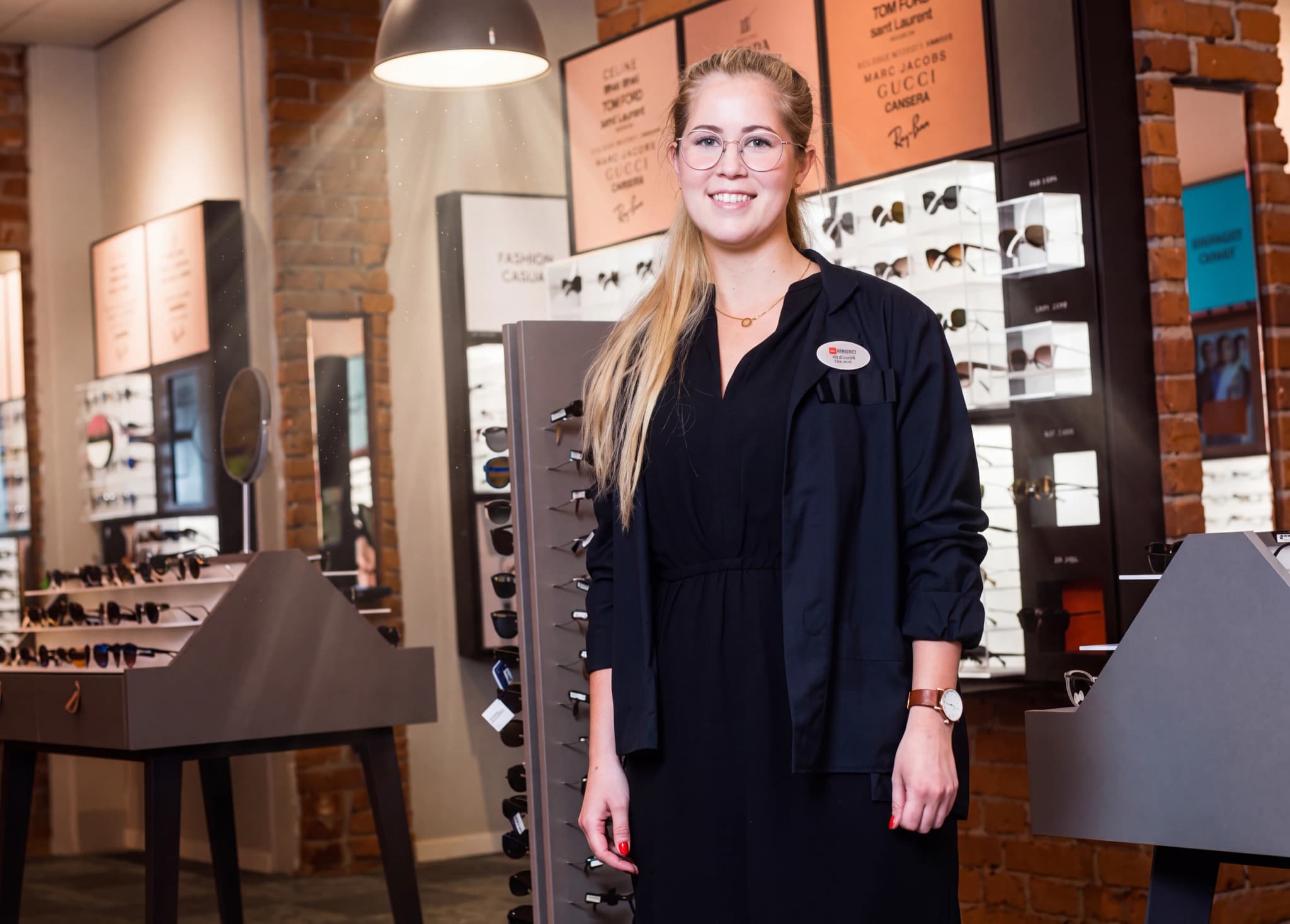 En leende kvinna med glasögon står i en optikerbutik.