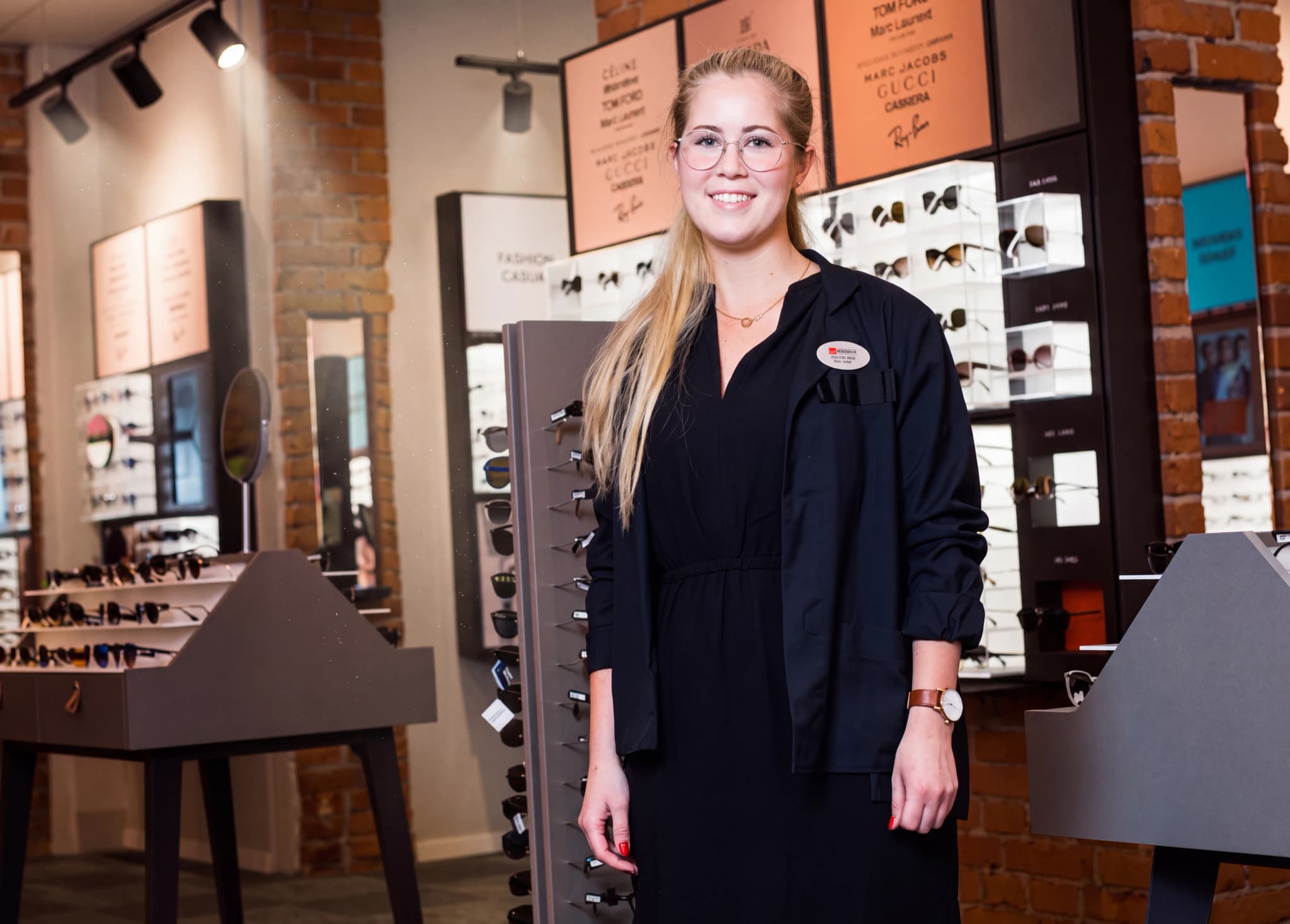 En leende ung kvinna som arbetar som optiker poserar i en butik som säljer glasögon.
