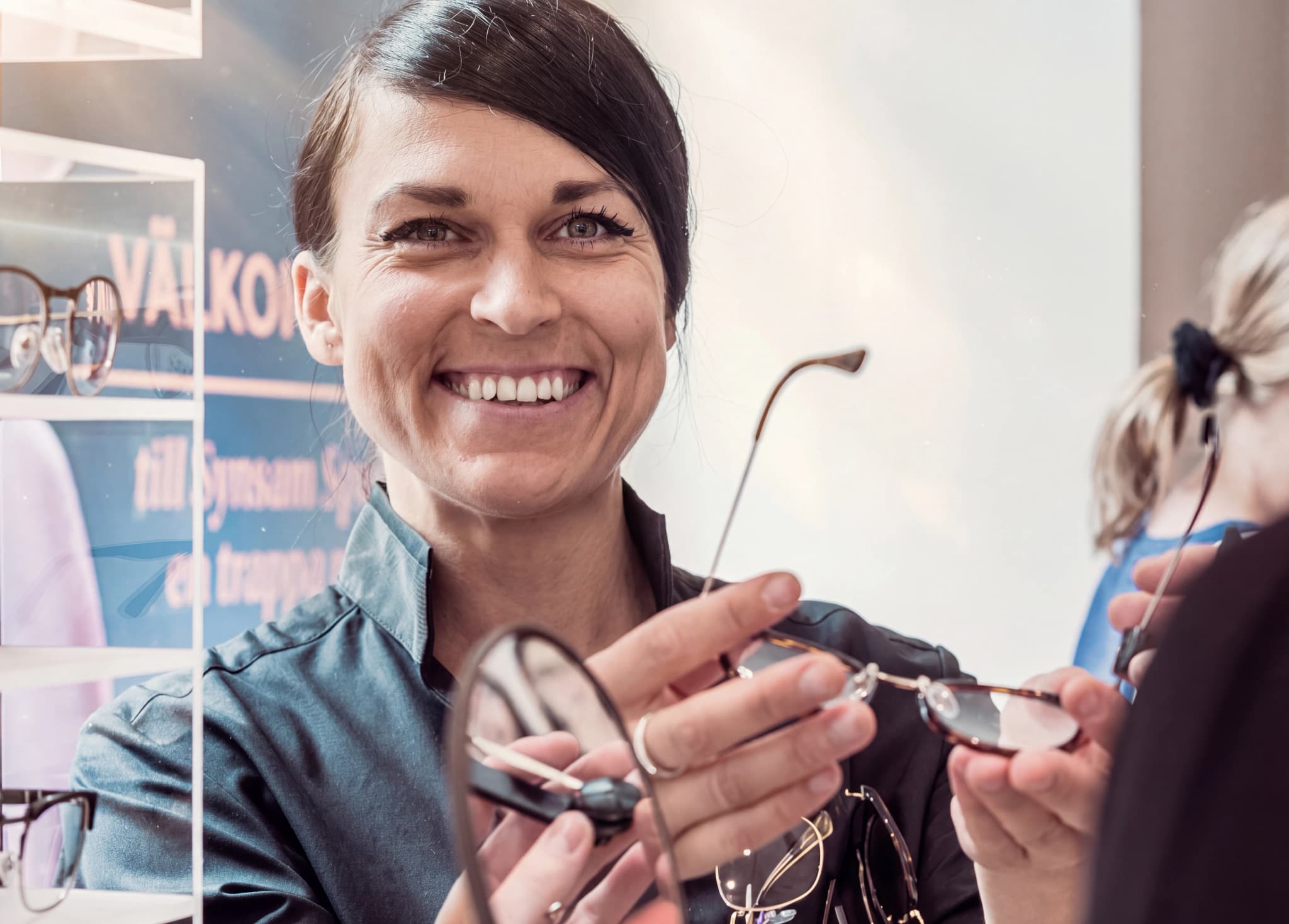 En optiker ler och visar ett par glasögon för en kund i en butik.