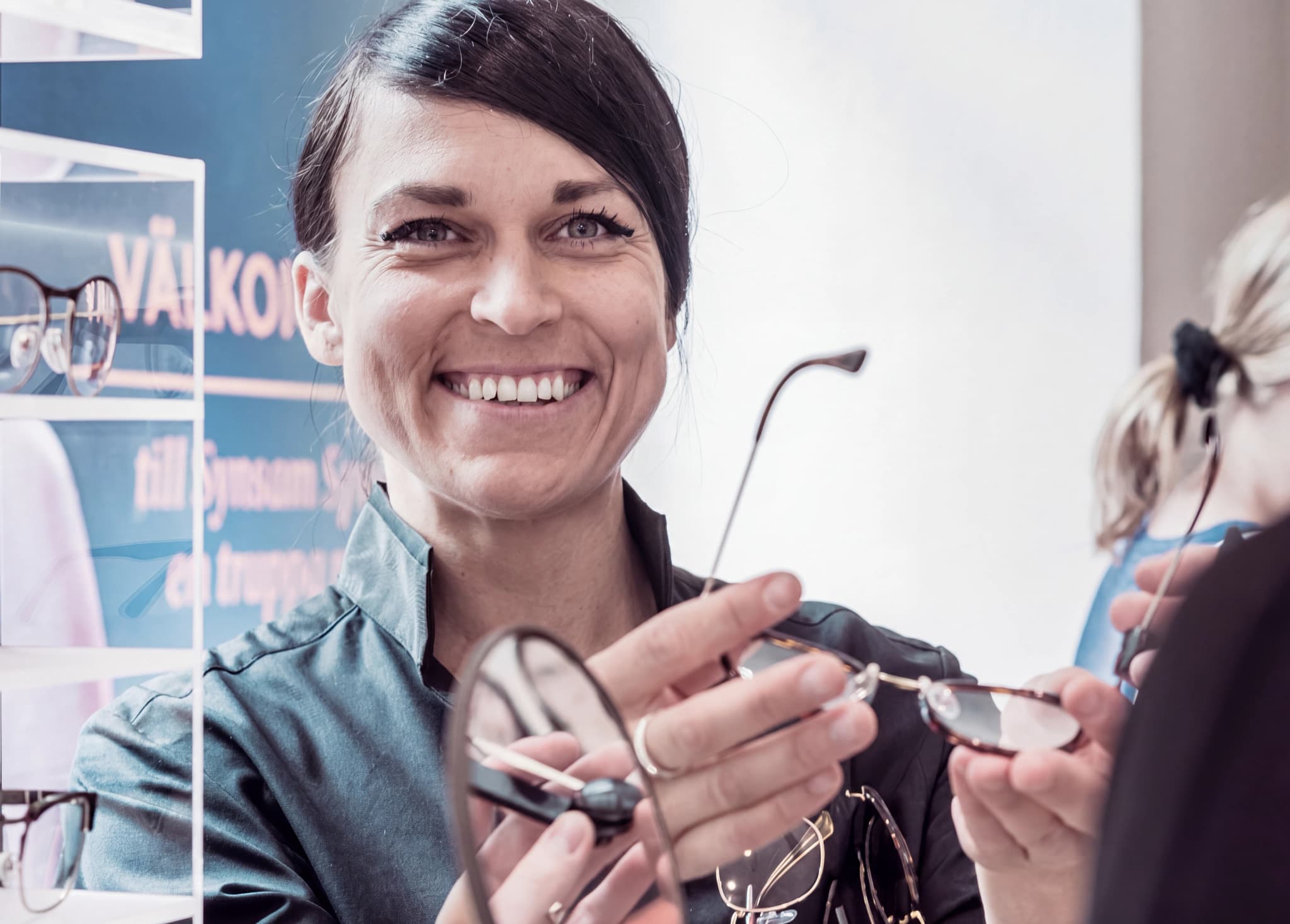 En leende optiker håller upp ett par glasögon för att visa en kund.