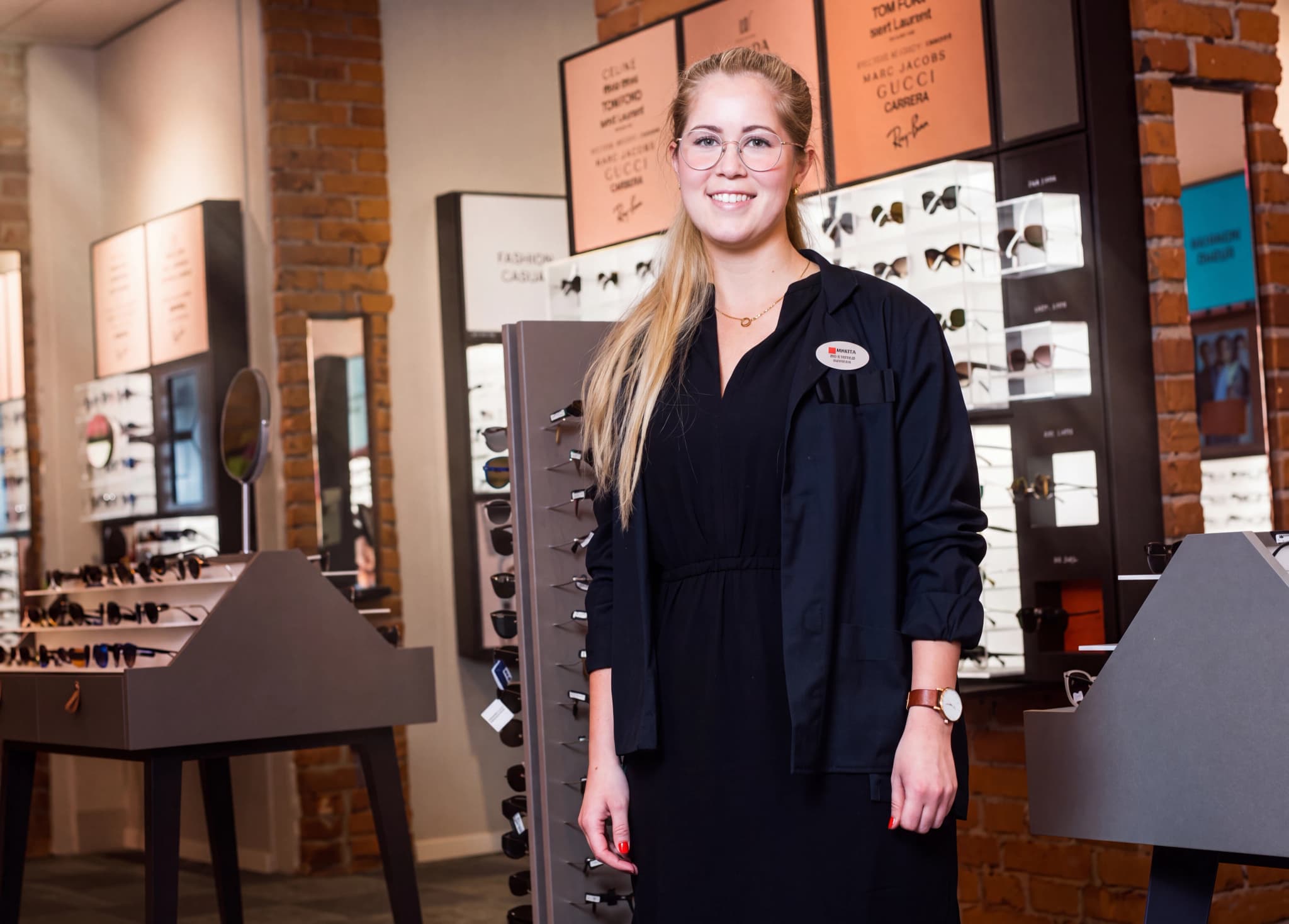 En ung kvinna med glasögon står i en butik som säljer glasögon och solglasögon.