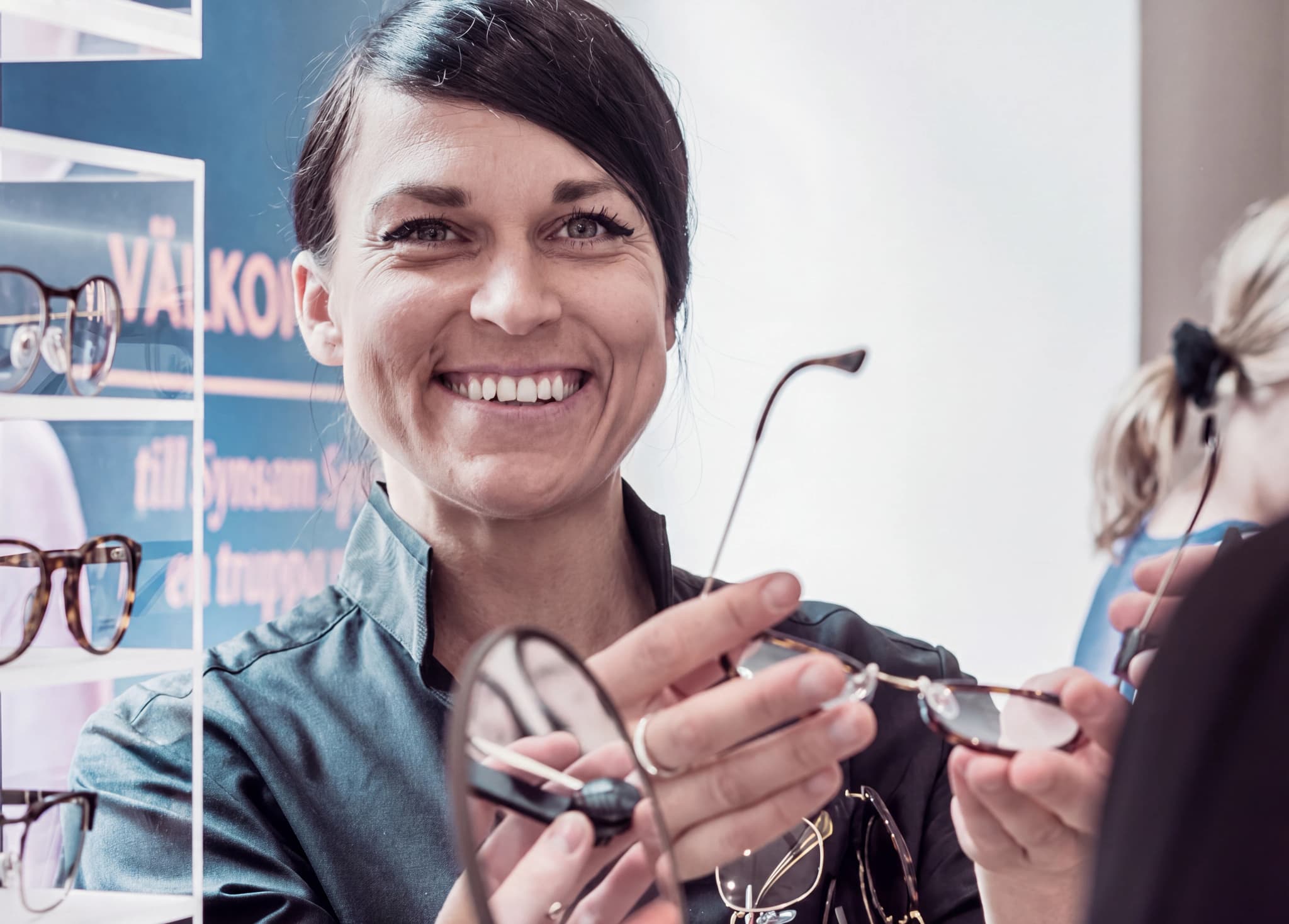 Optiker visar glasögon för en kund i en butik med displayer av glasögon.
