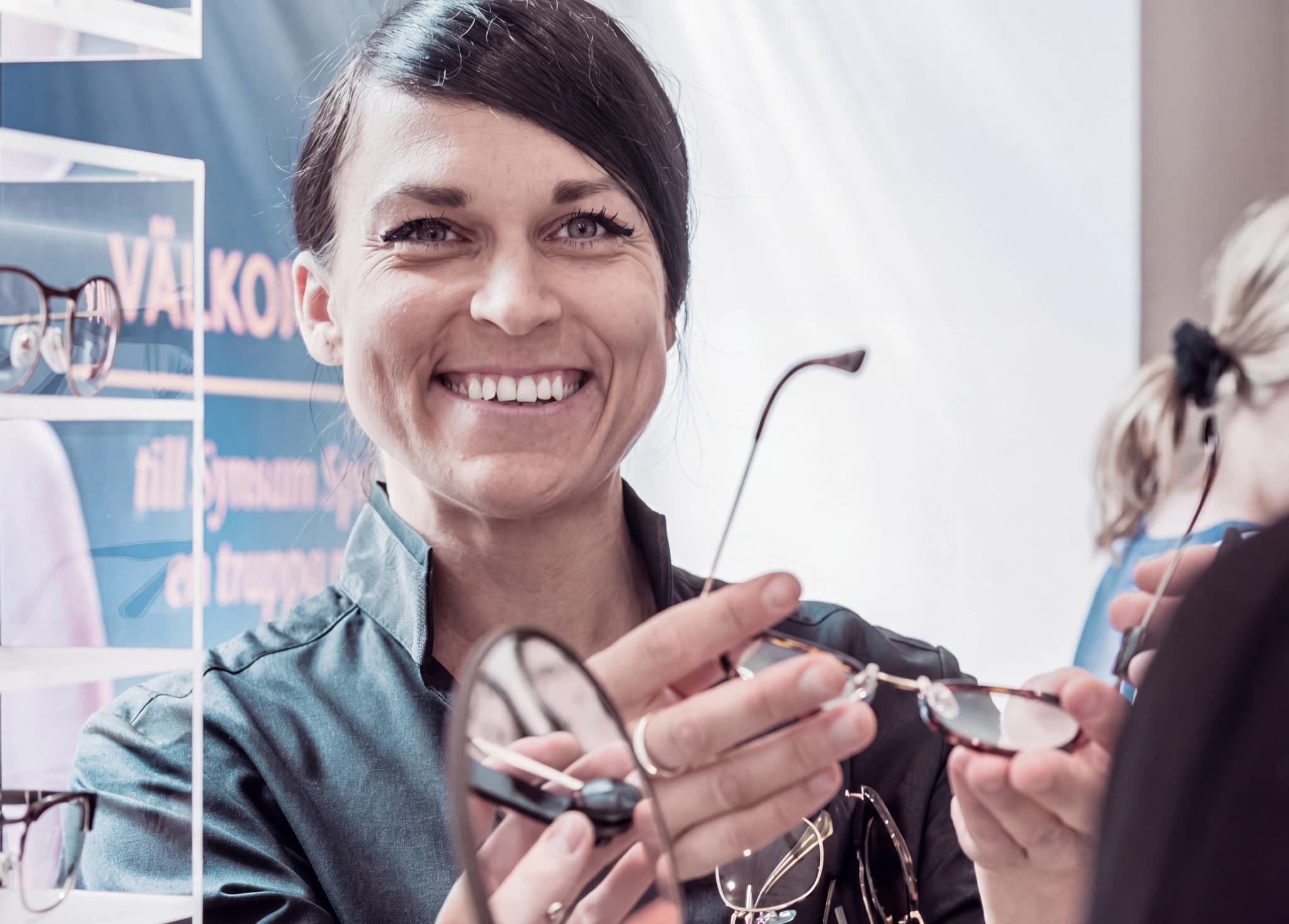 Optiker ler medan hon håller upp ett par glasögon för att visa en kund.