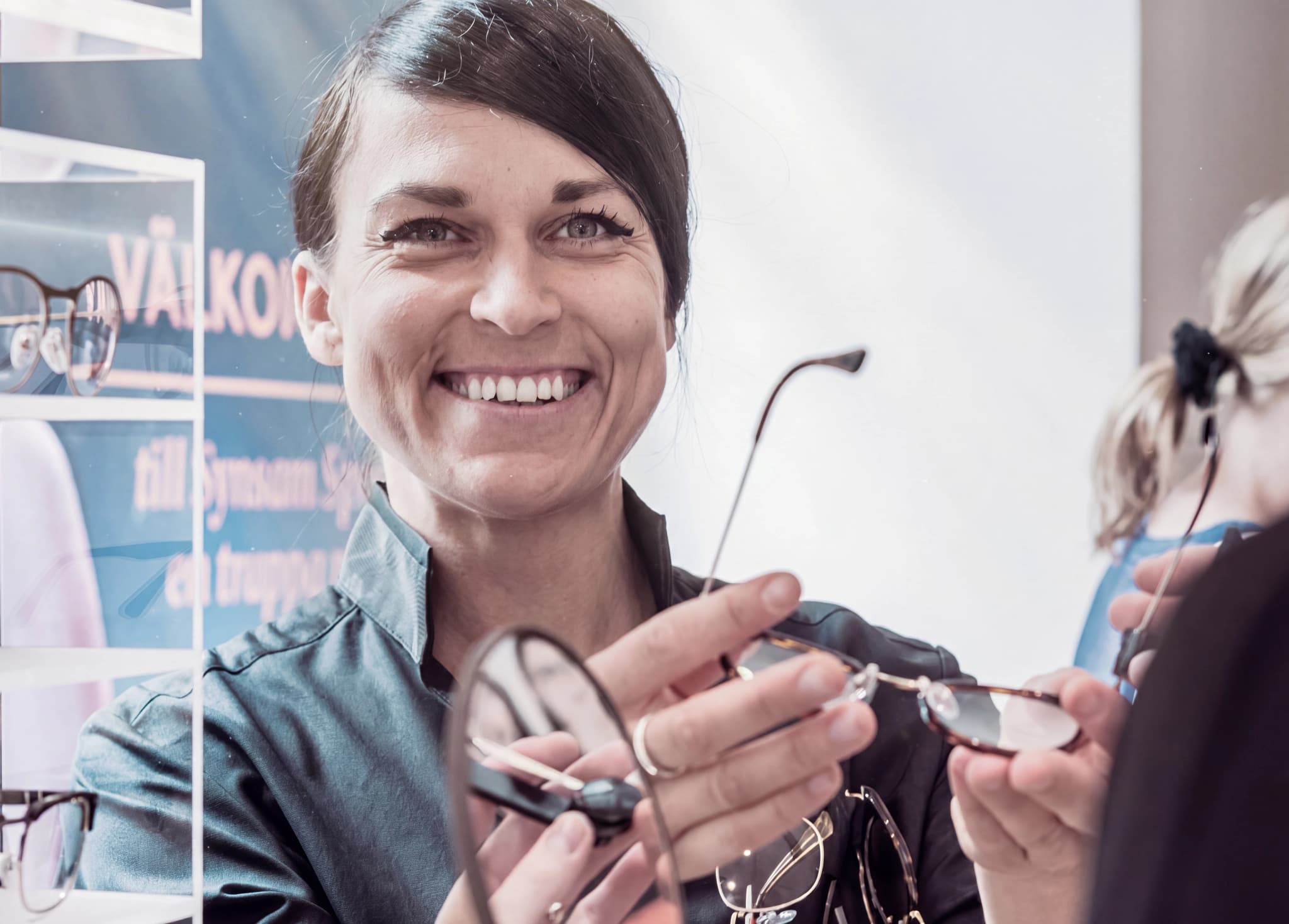 En leende optiker håller upp ett par glasögon för en kund.