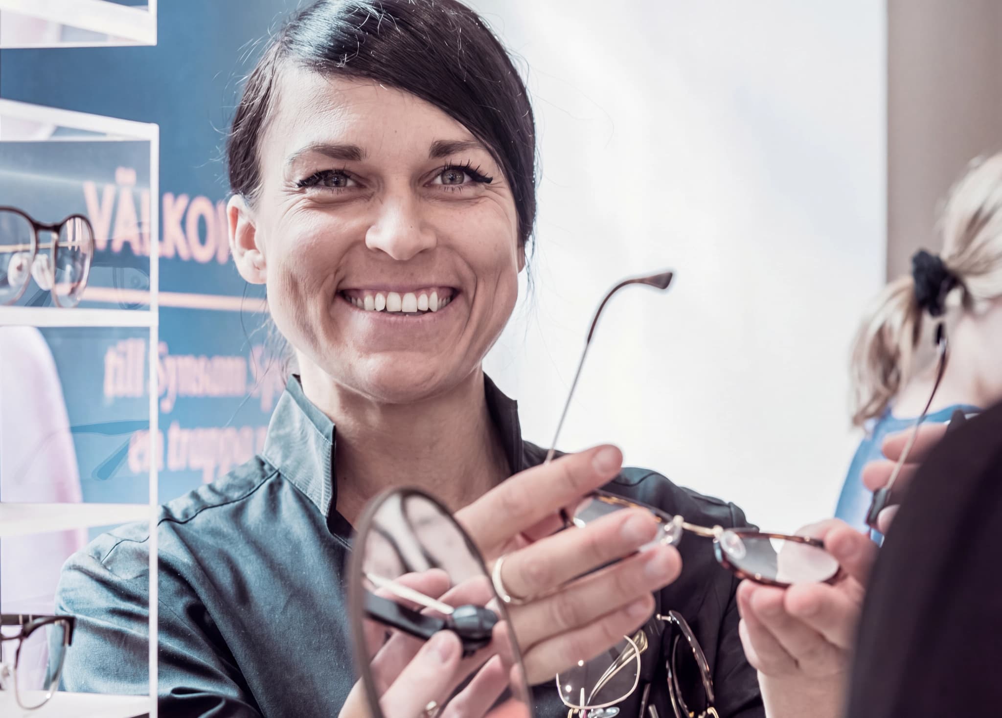En optiker visar upp ett par glasögon för en kund i en butik.