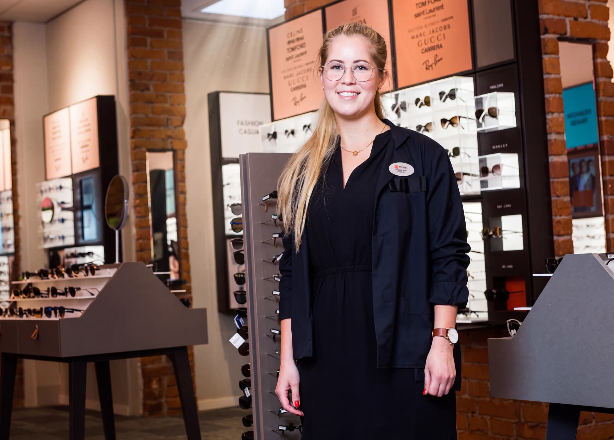 En ung kvinna med glasögon och en svart jacka som arbetar i en butik som säljer glasögon och solglasögon.