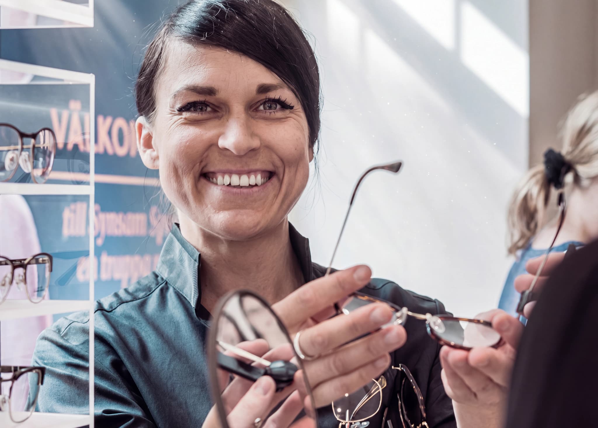 Optiker ler och visar glasögon för en kund i en butik.