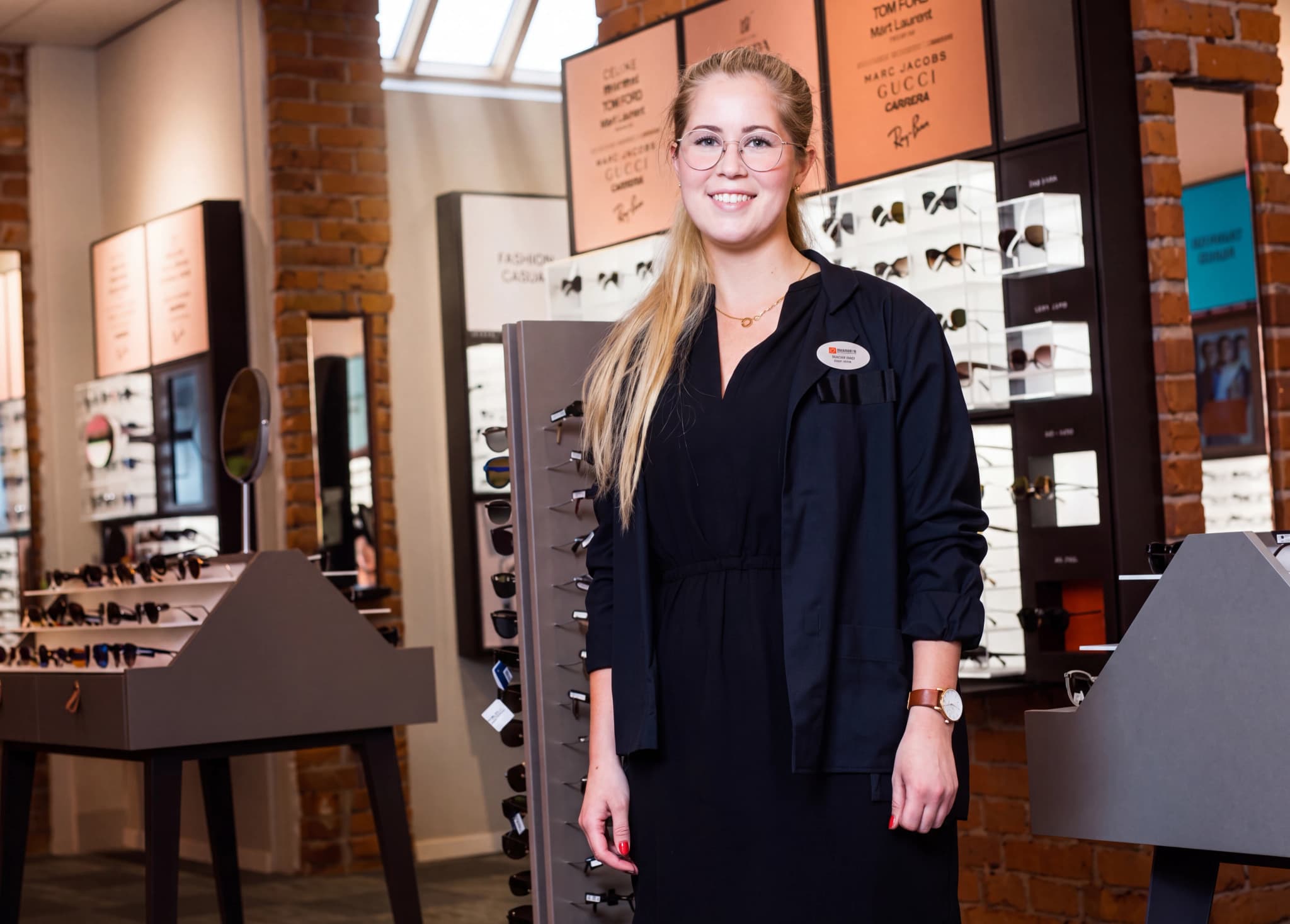 Optiker står i en optikerbutik och ler mot kameran.