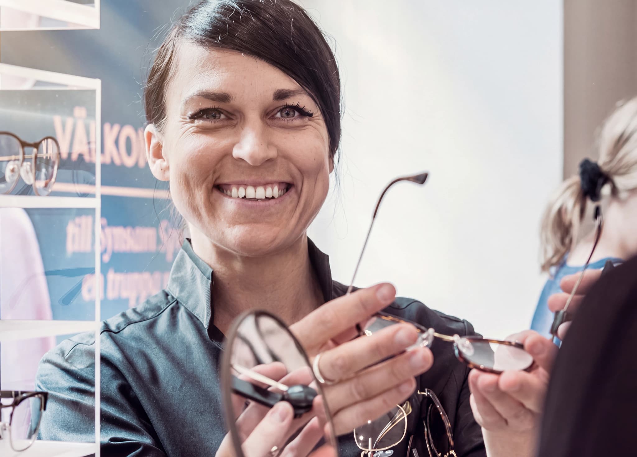 Optiker ler och visar upp glasögon för en kund i en butik.