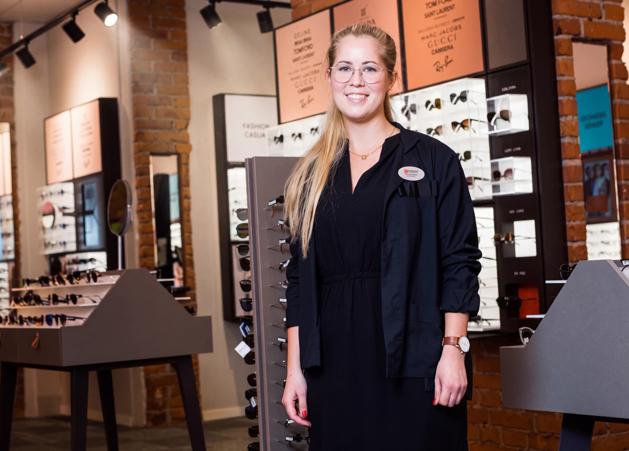 En leende ung kvinna som arbetar som optiker står i en butik som säljer glasögon.