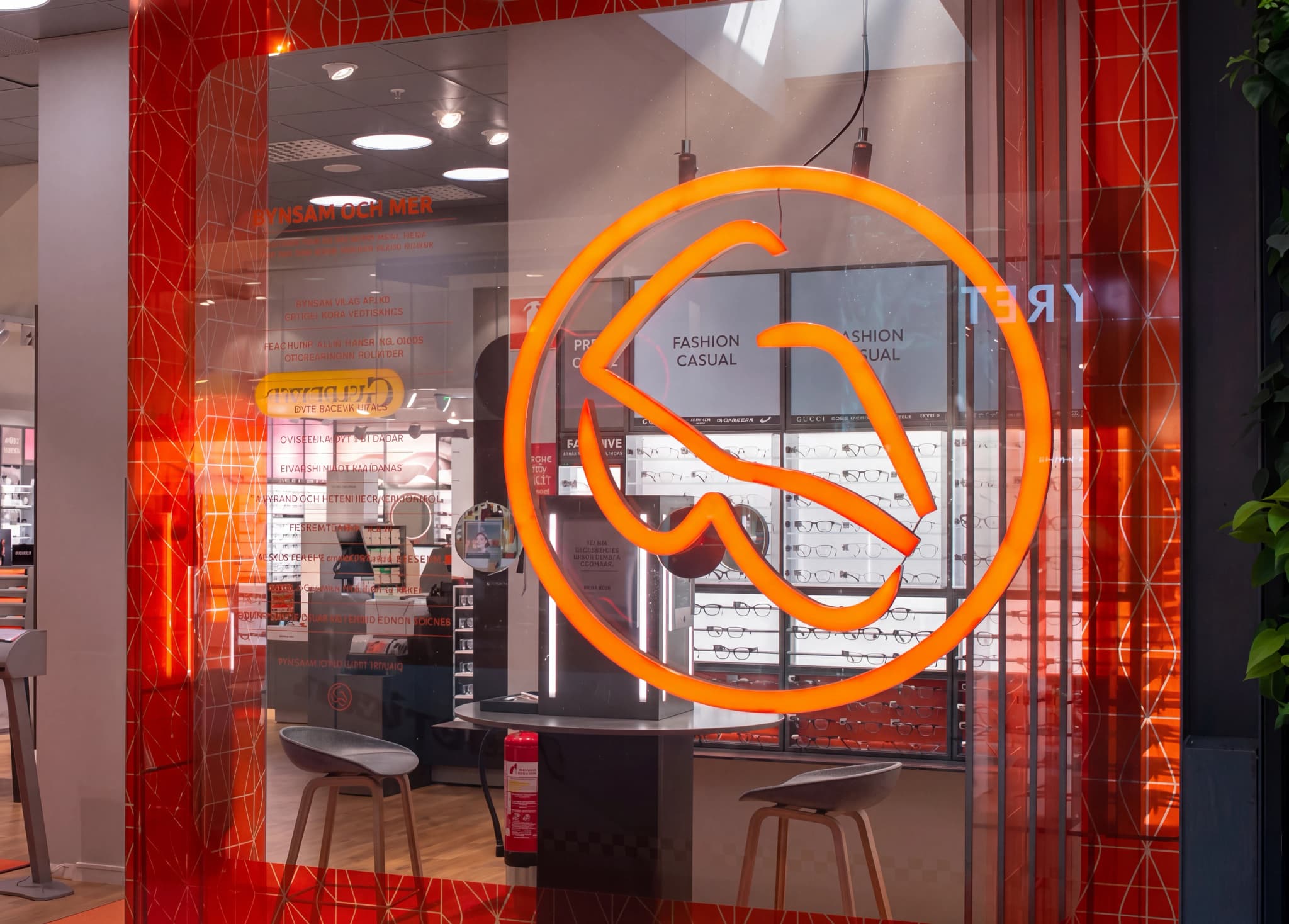 Butiksfasad för en optiker med en stor orange logotyp och skyltar med 'FASHION CASUAL'.