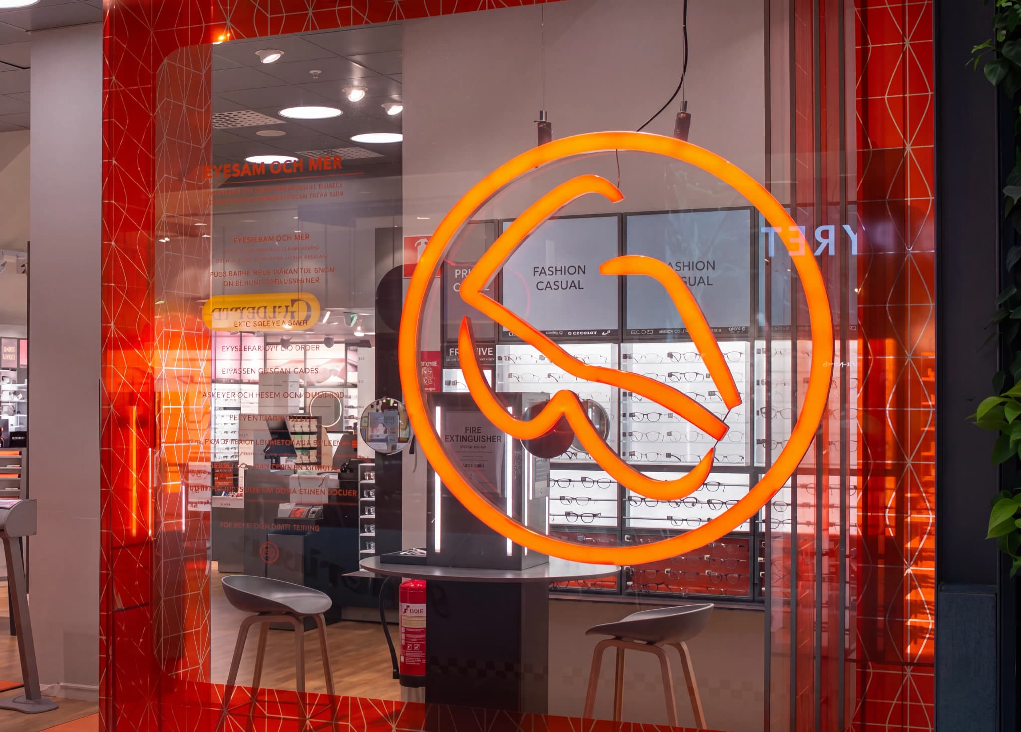 Butiksfasad med en stor orange logotyp i neonstil och displayer med glasögon och reklambudskap.