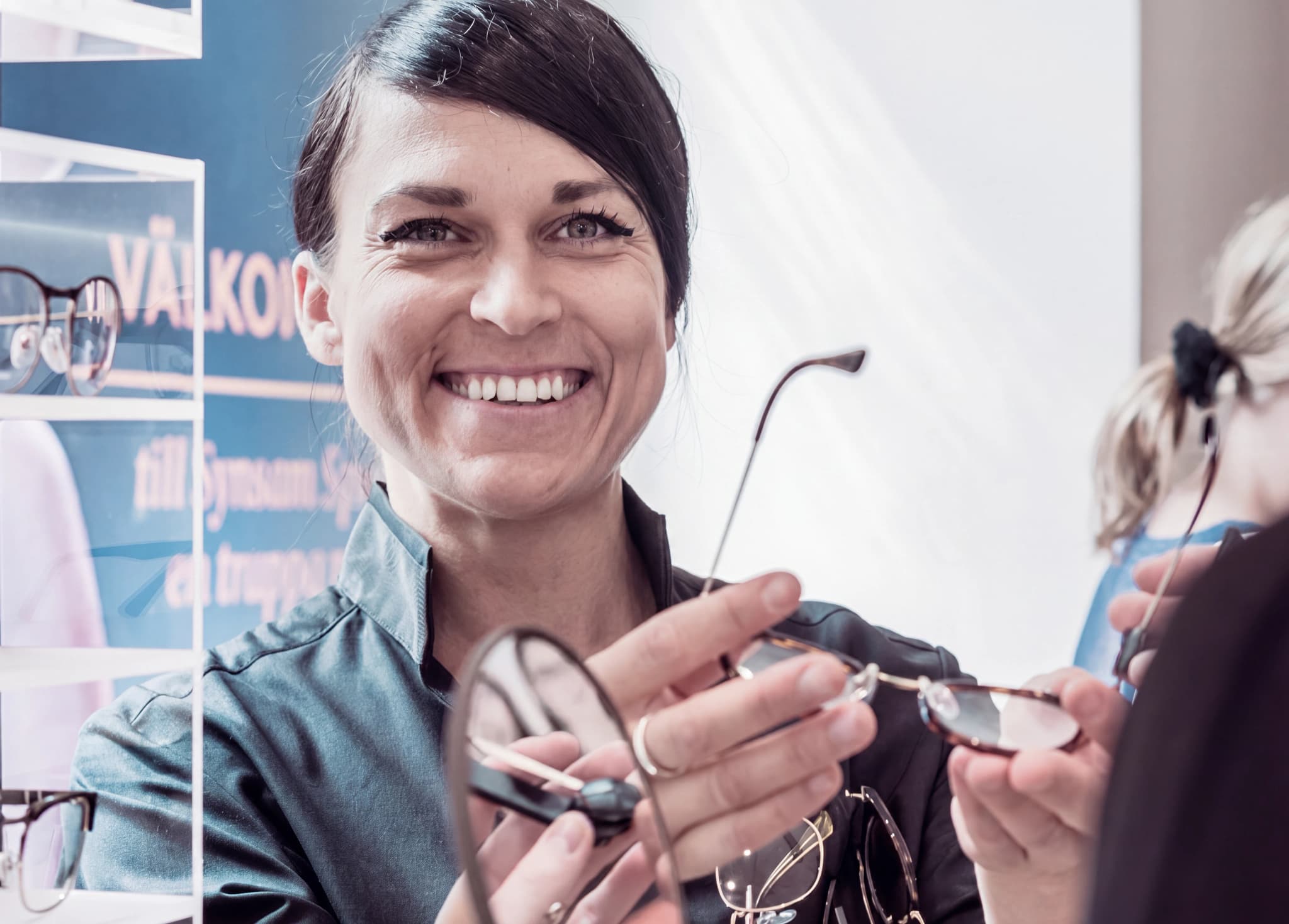 Optiker som håller upp ett par glasögon för en kund i en butik