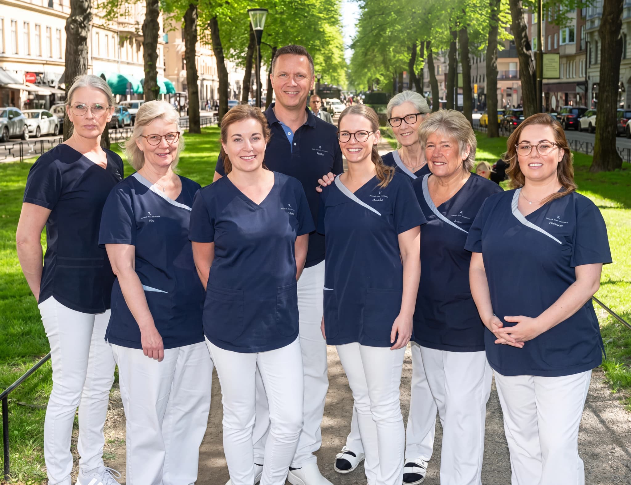 Grupp av åtta sjukvårdspersonal, sex kvinnor och två män, som poserar utomhus i uniform.