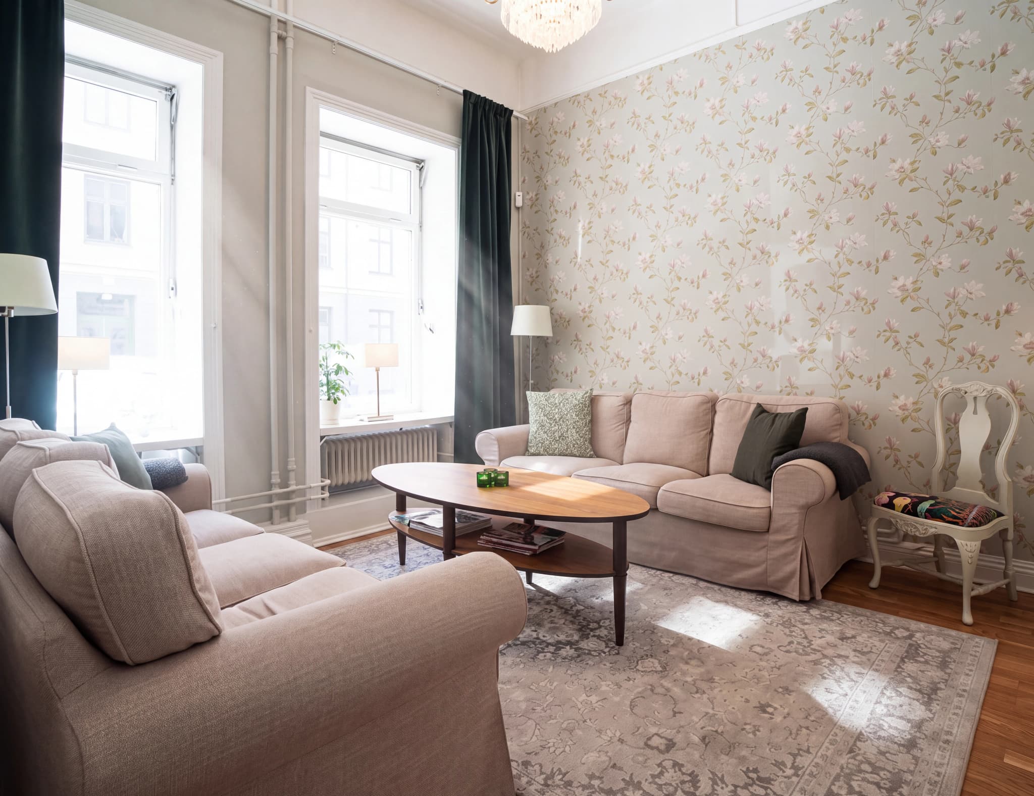 Ett vardagsrum med en blommig tapet, en bekväm soffa, ett soffbord och en matta.