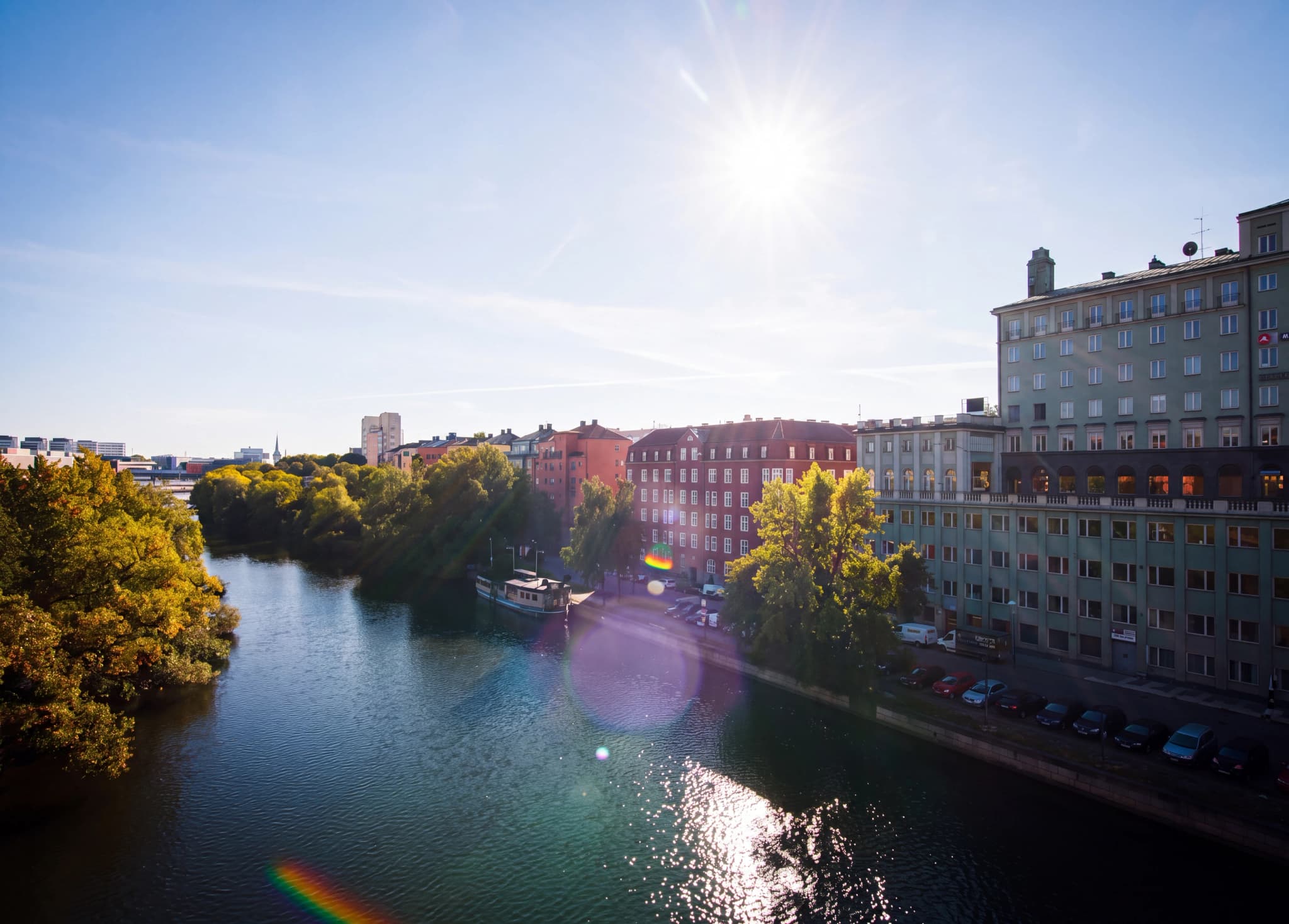 Byggnader längs en flod en solig dag med solreflexer i vattnet.