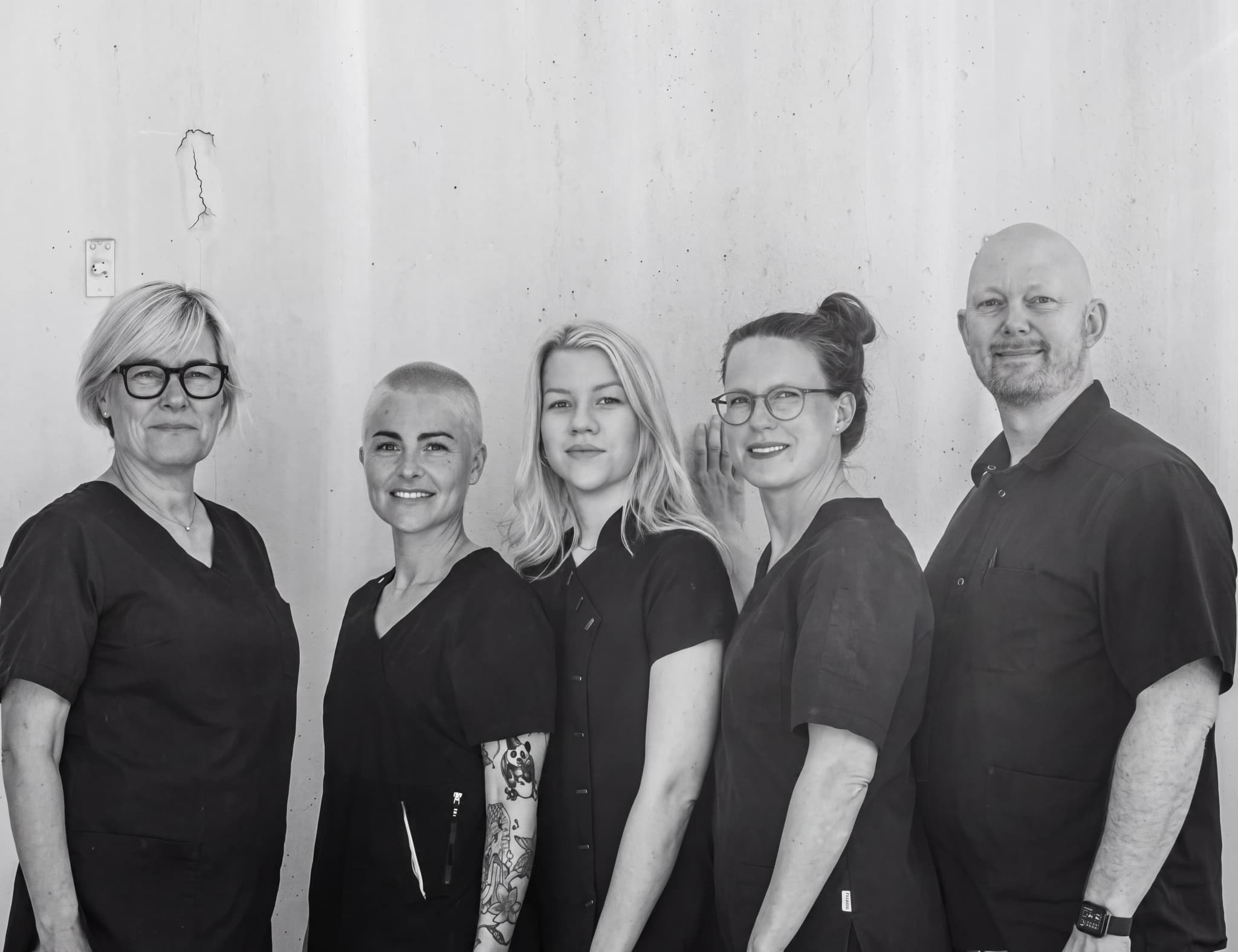Gruppbild på fem leende vårdpersonal som står framför en slät vägg.