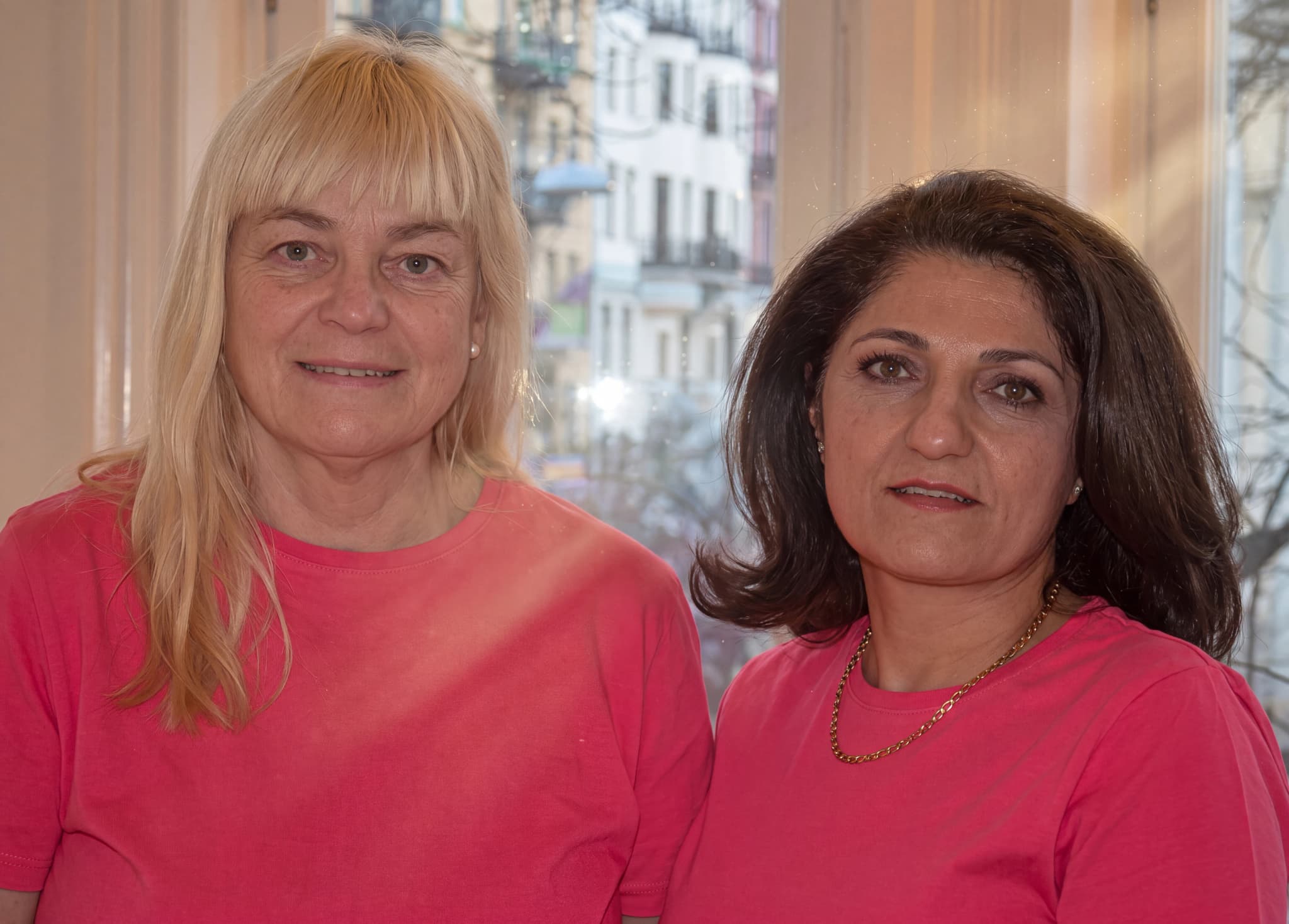 Två kvinnor i rosa toppar som poserar för en bild.