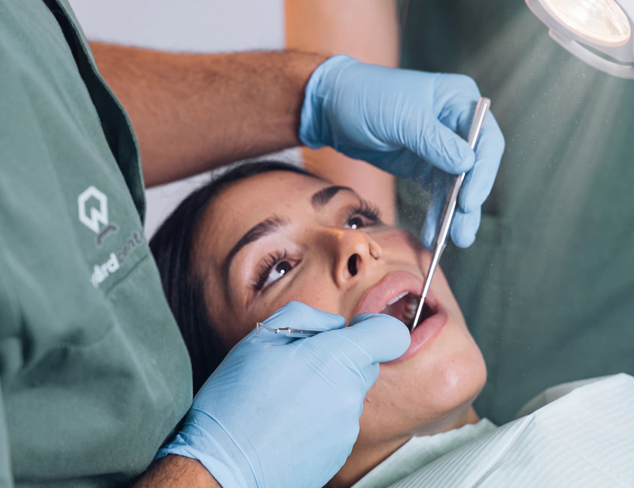 Tandläkare med ljusblå handskar undersöker en kvinnlig patients tänder med tandvårdsredskap.