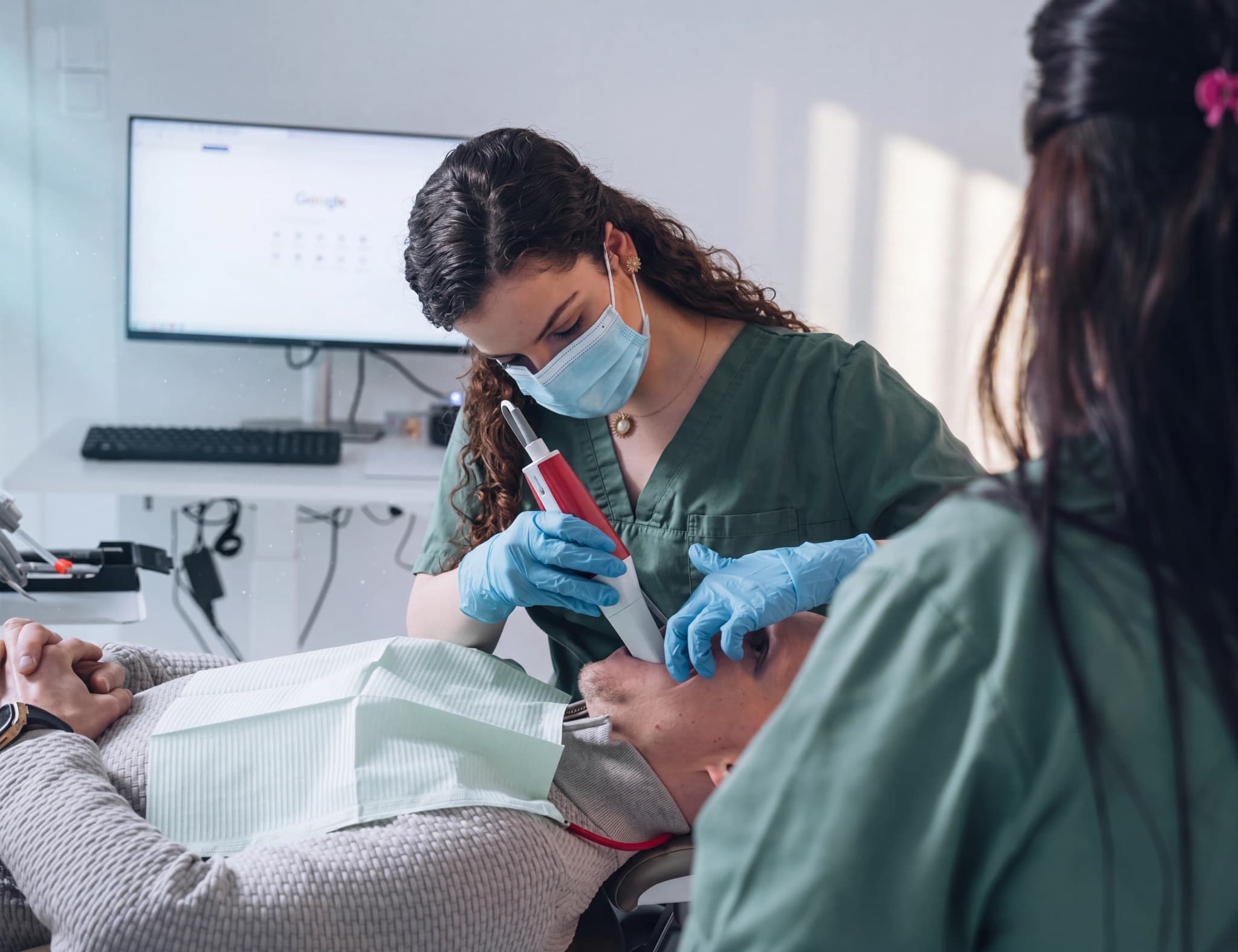 Tandläkare med munskydd och handskar använder en dentalscanner på en patient som ligger i en tandläkarstol.