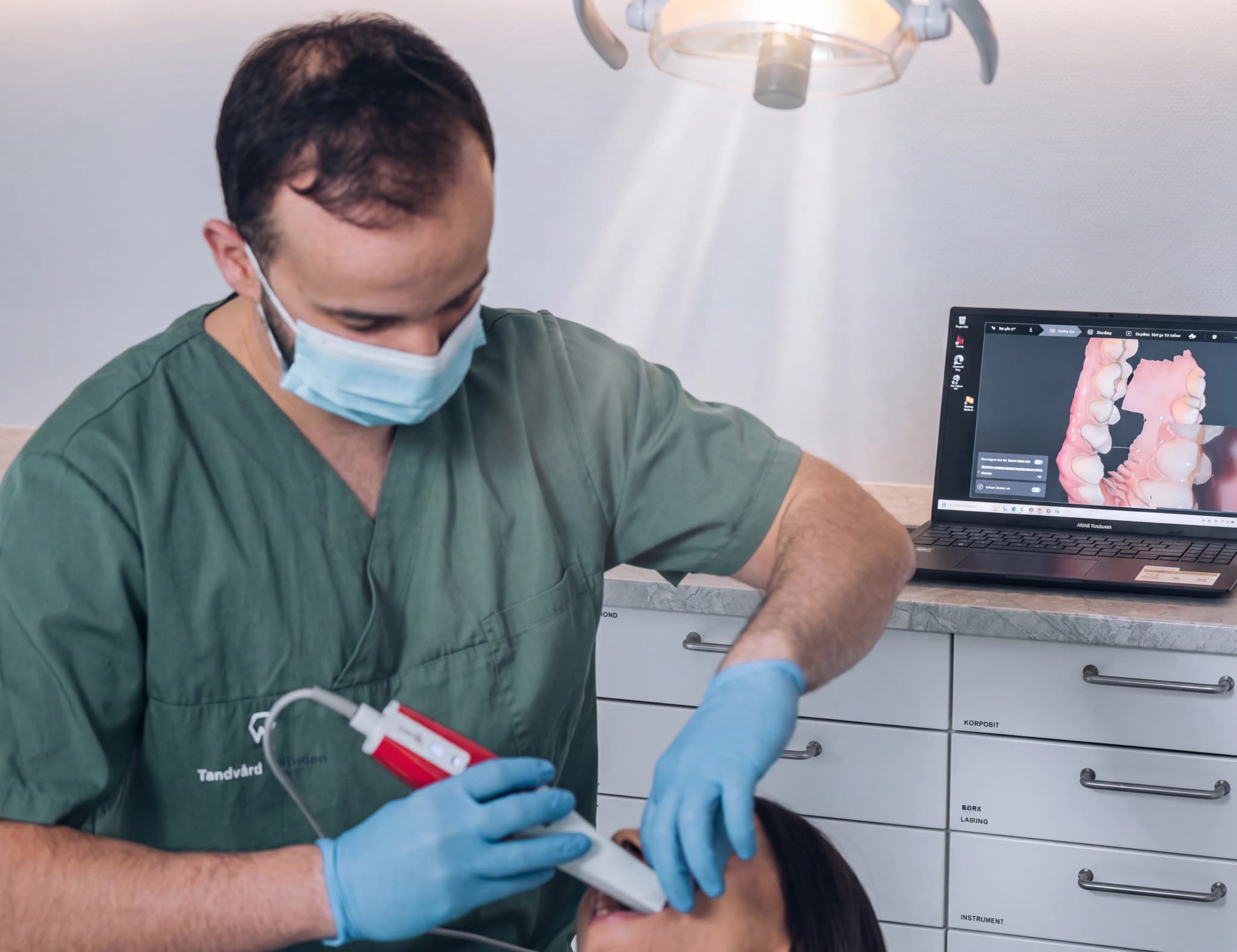 Tandläkare med en intraoral skanner som skannar en patients tänder och skapar en digital modell på en bärbar datorskärm.