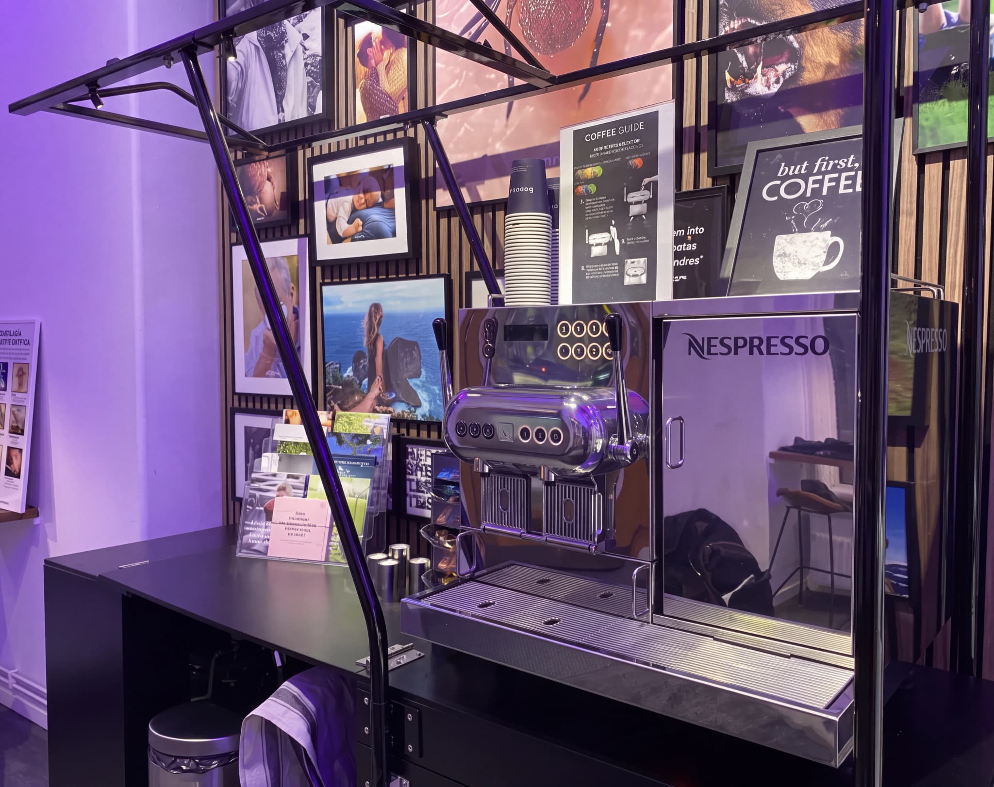 En Nespresso kaffemaskin på en disk med foton och illustrationer på väggen bakom.