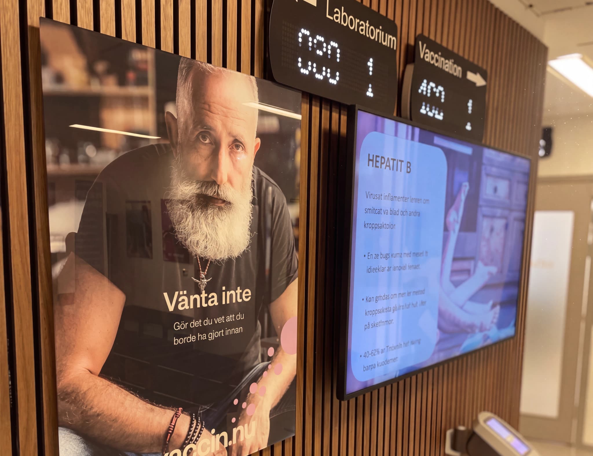 Affisch med en man med långt vitt skägg som har texten 'Vänta inte. Gör det du vet att du borde ha gjort innan' och en informationsskärm om Hepatit B.